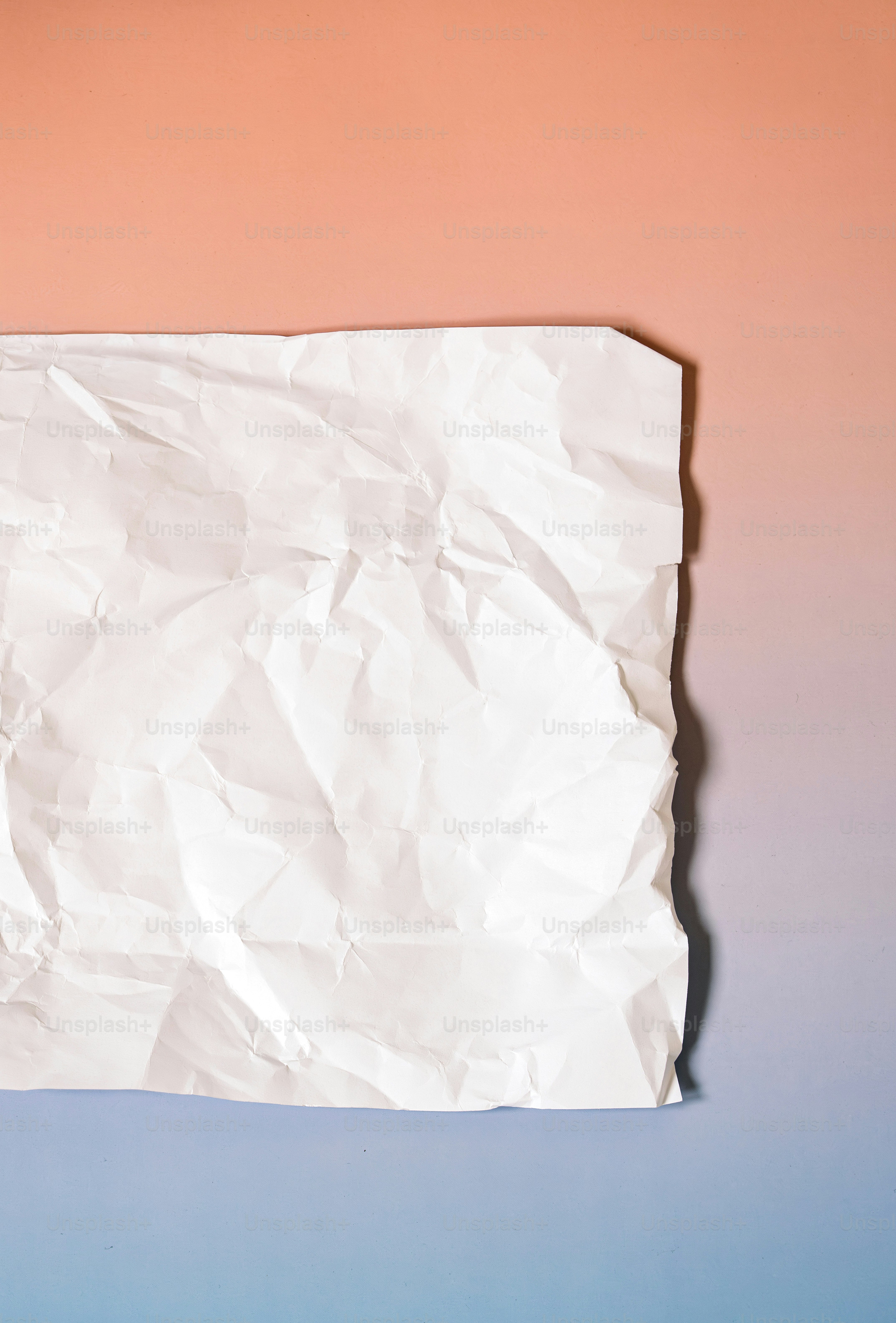 Papier blanc froissé sur fond dégradé pêche et bleu.