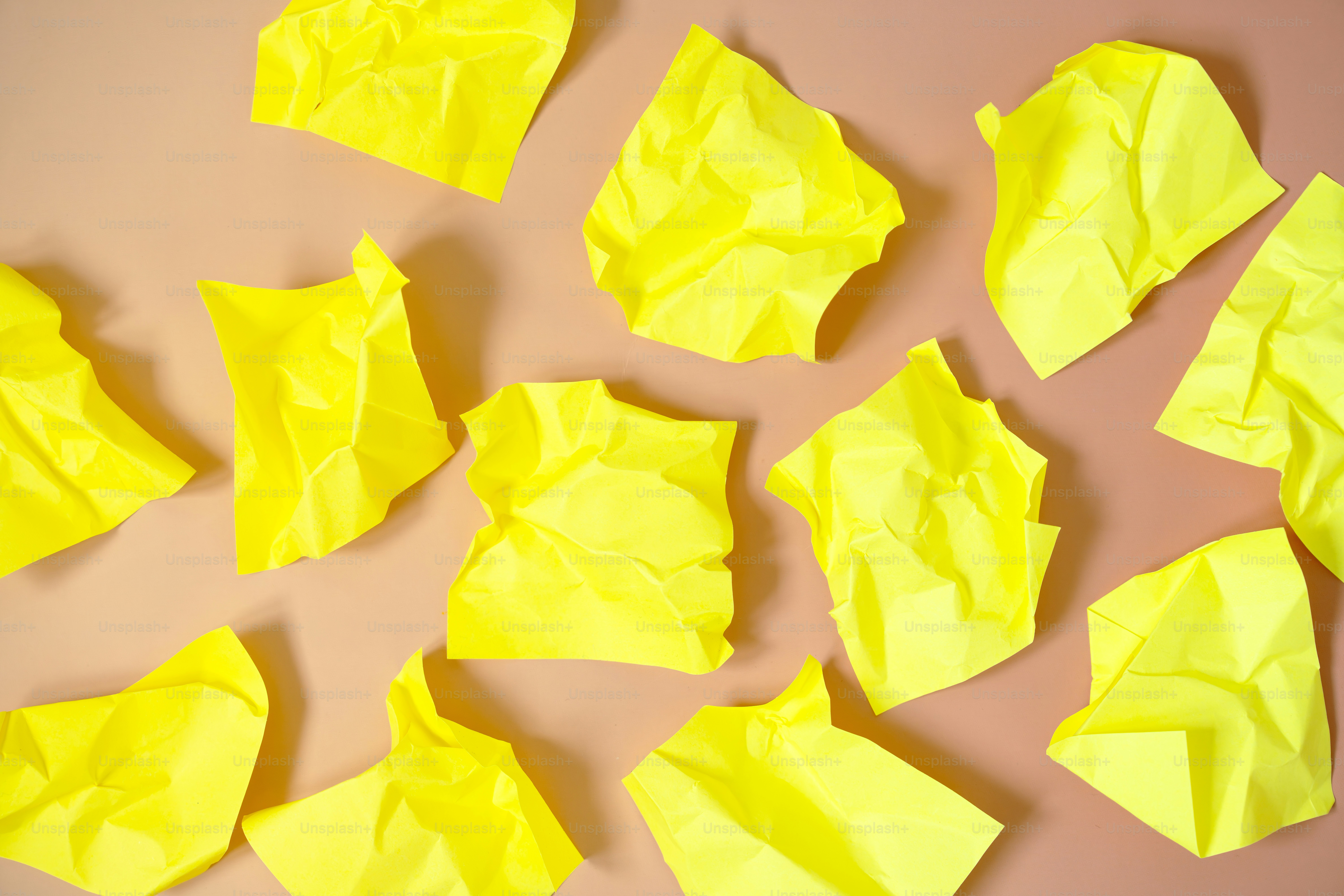 Des morceaux de papier jaune froissés éparpillés sur un fond brun clair.