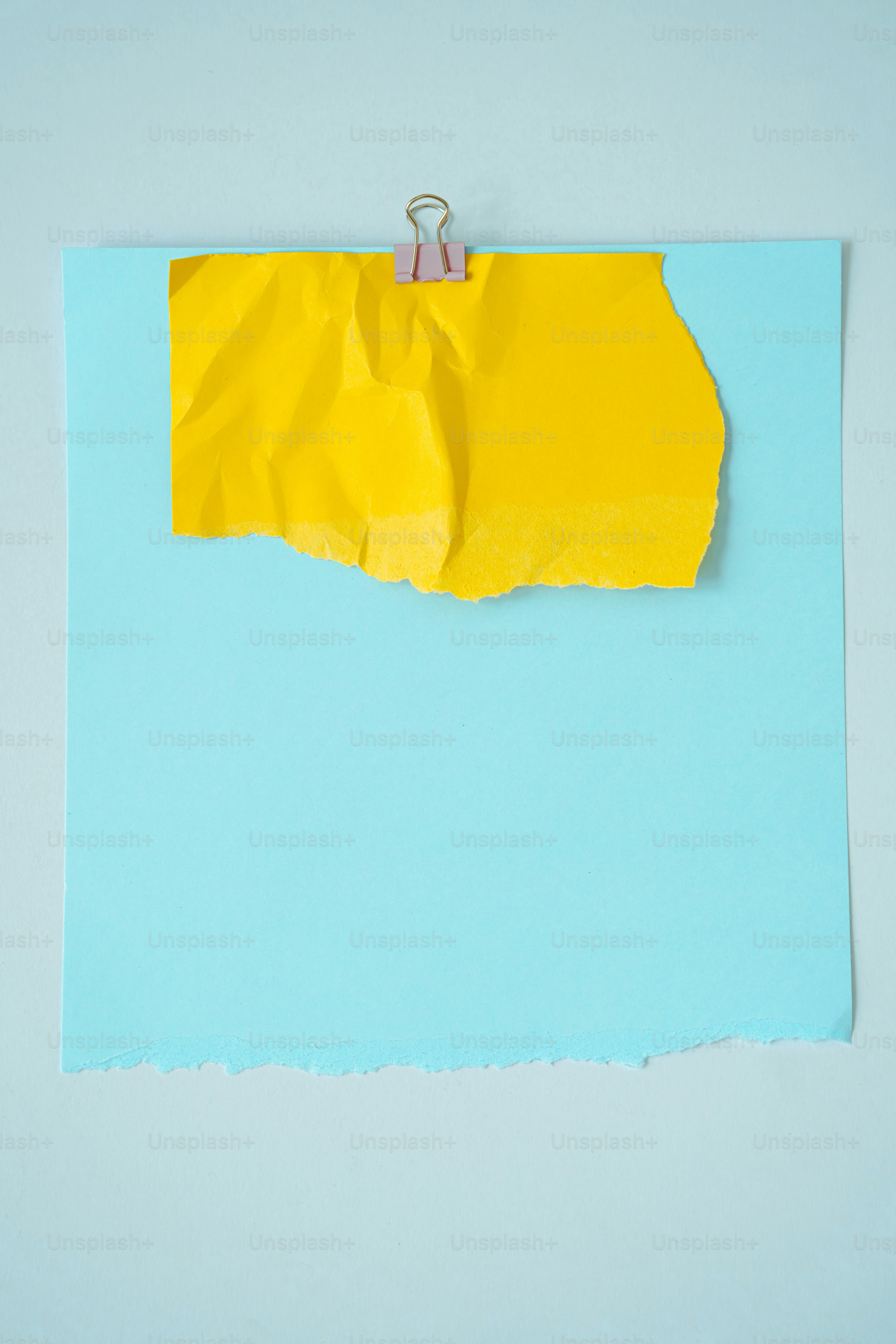 Papier jaune froissé clipsé sur un fond bleu clair.