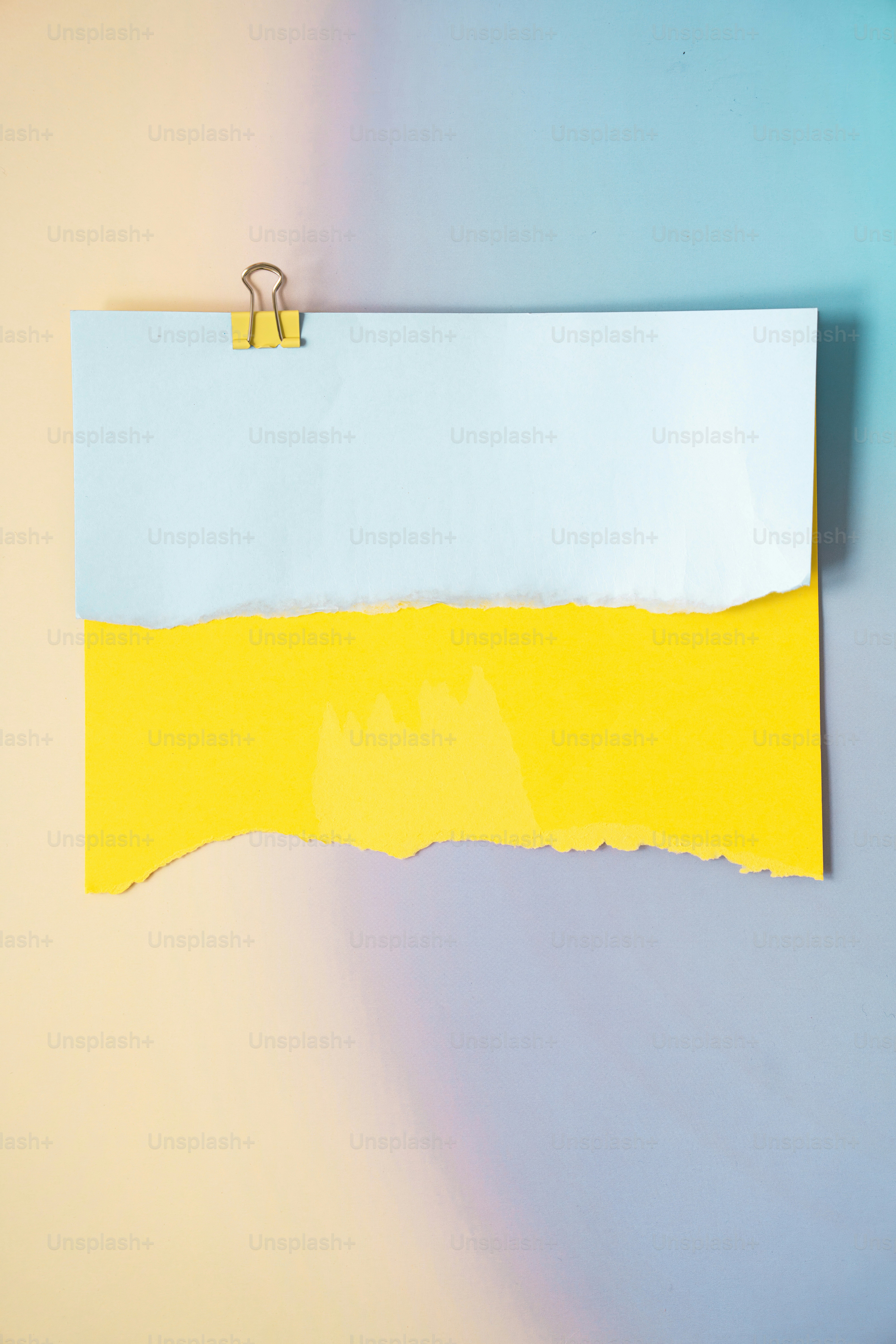 Du papier déchiré bleu clair et jaune tenu par une pince.