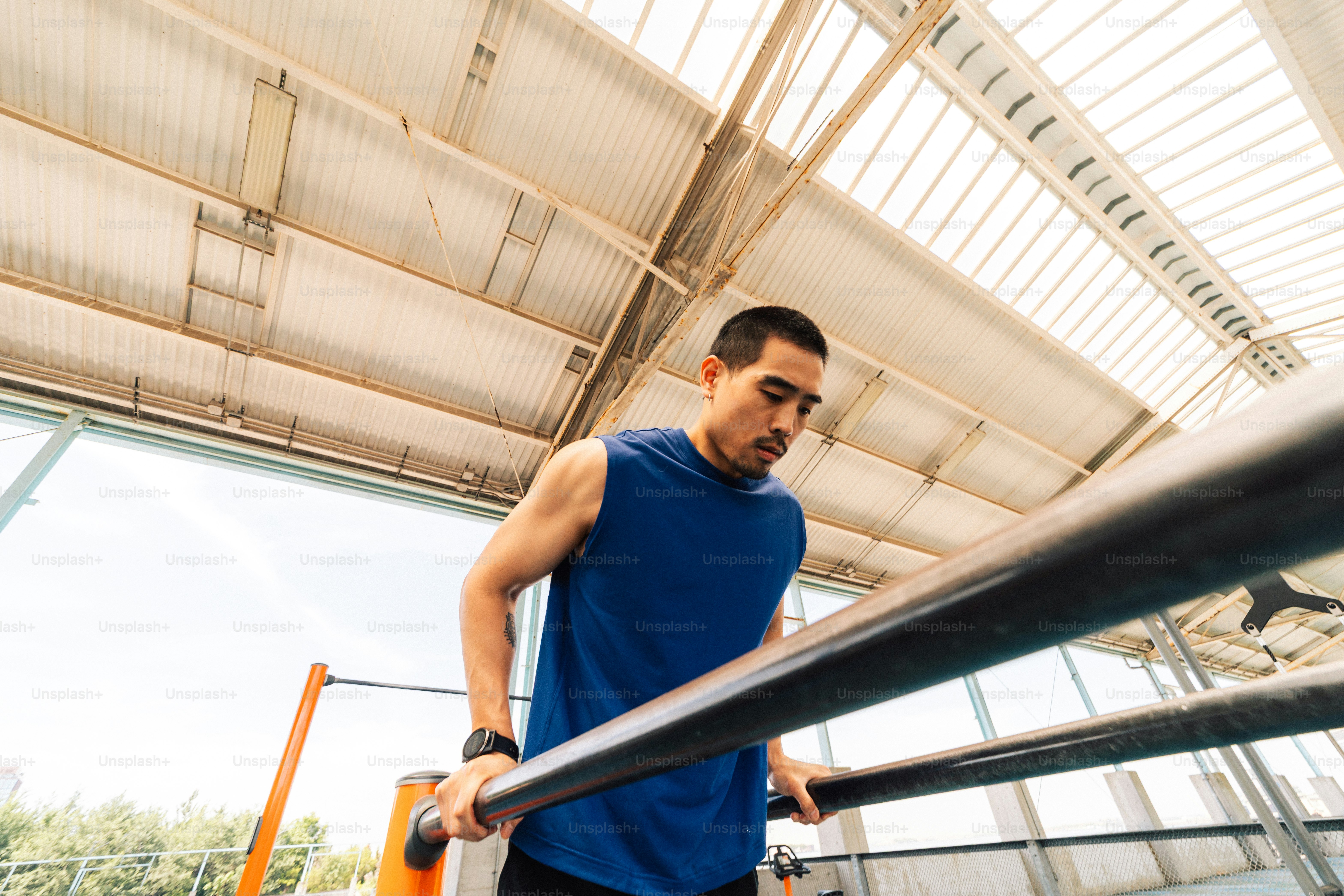 Pria berbaju tank top biru berolahraga di palang paralel.