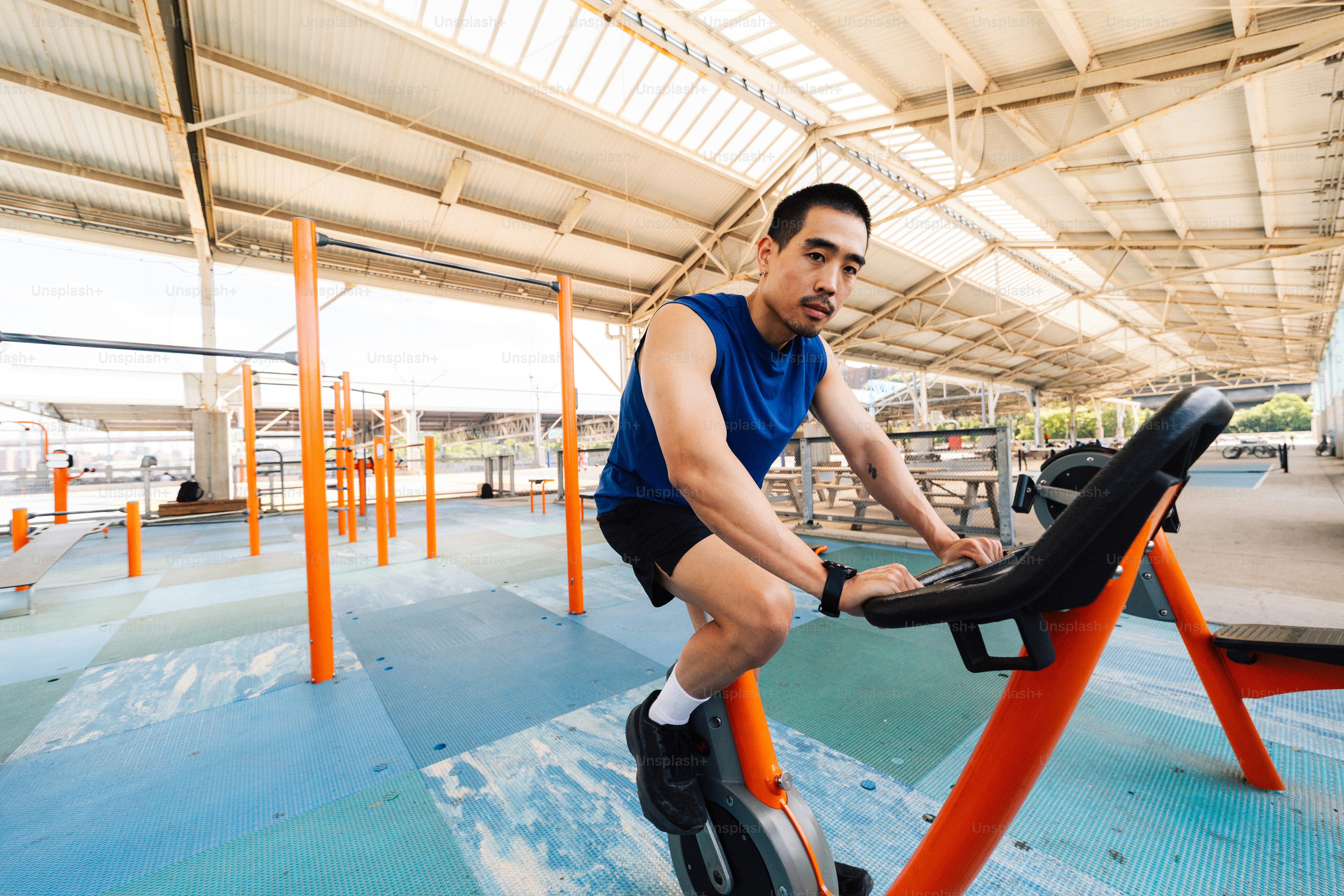 Pria berolahraga dengan sepeda statis di gym luar ruangan.