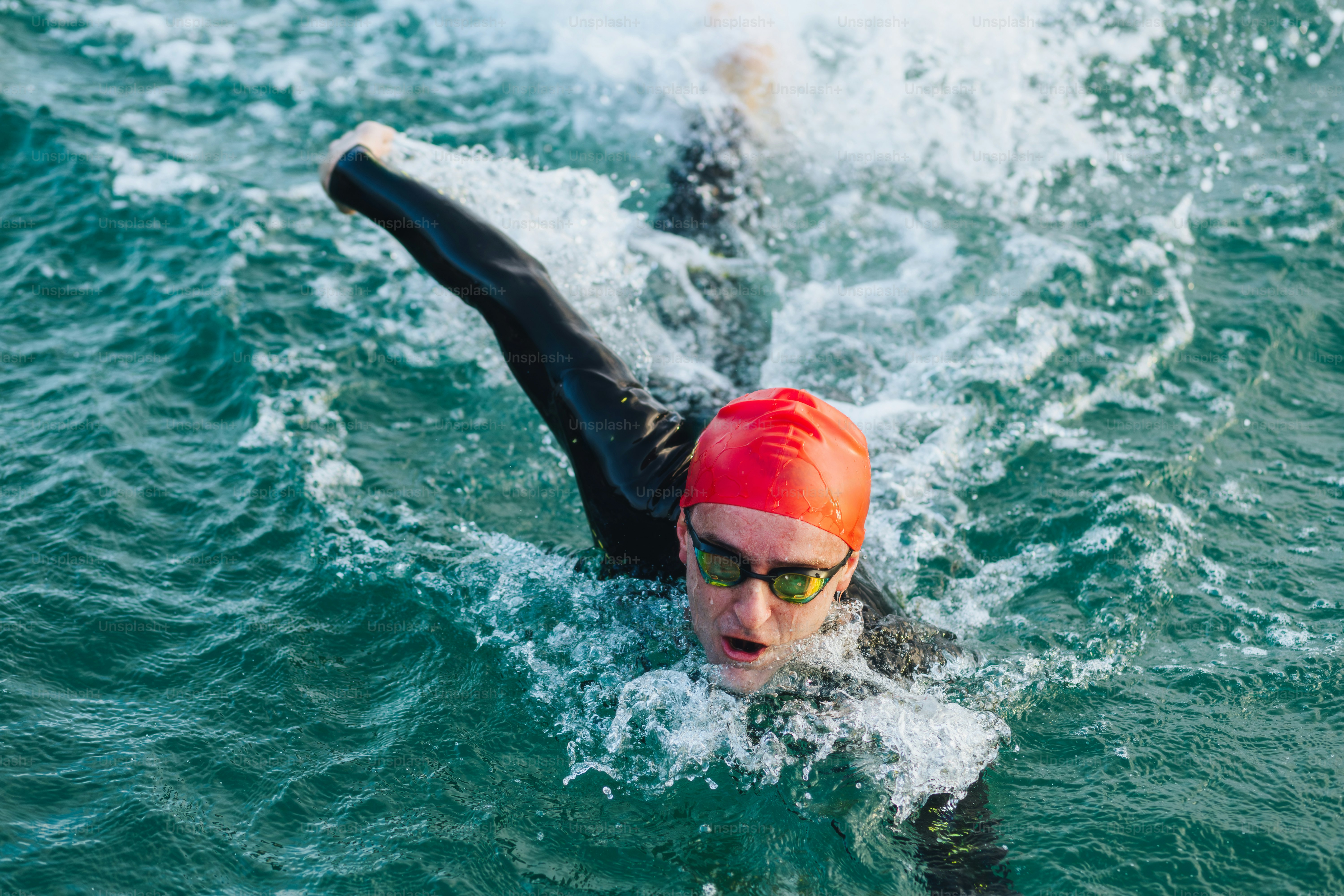 A person swimming in a wetsuit with a red cap