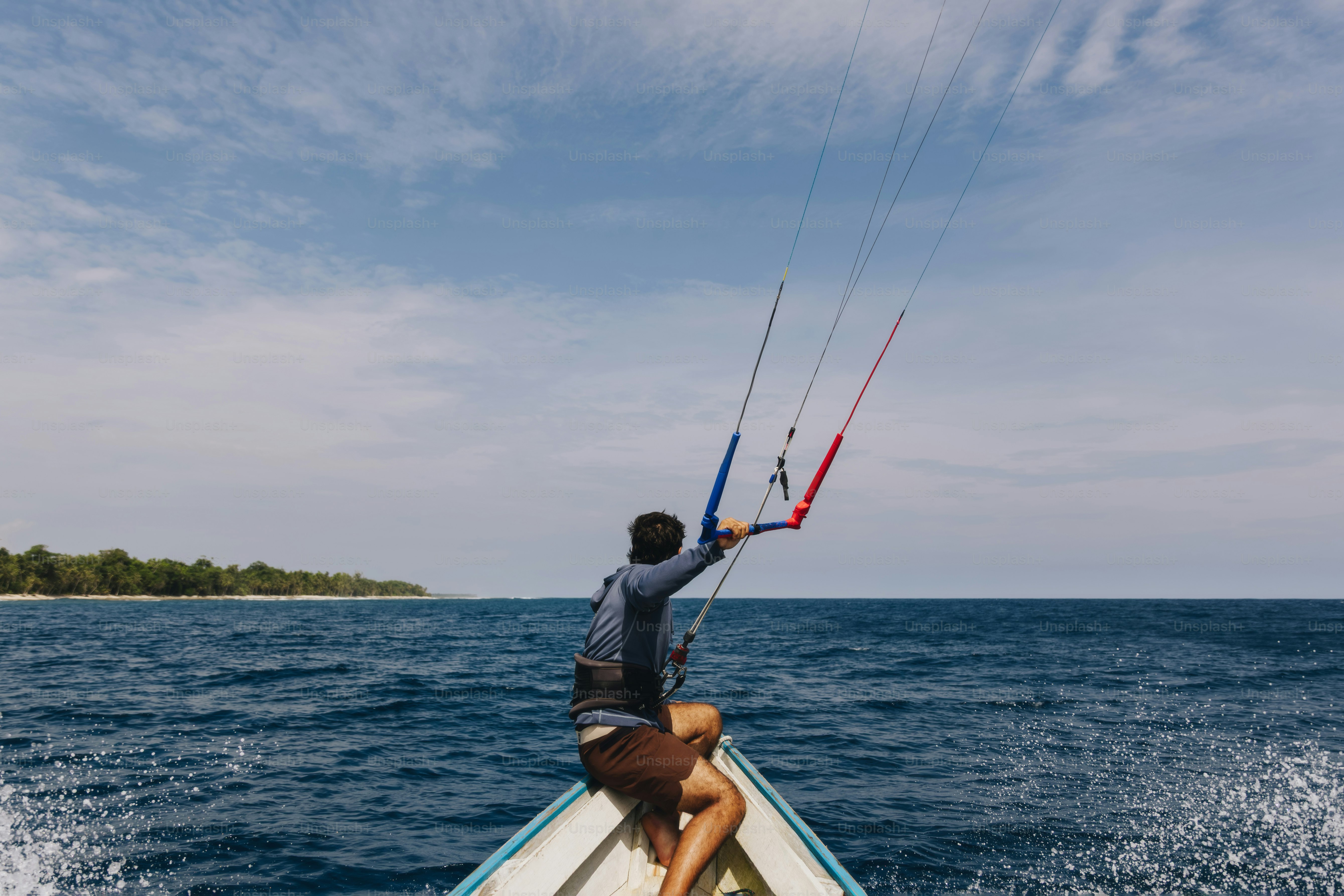 Man on boat holding kiteboarding gear on the blue ocean