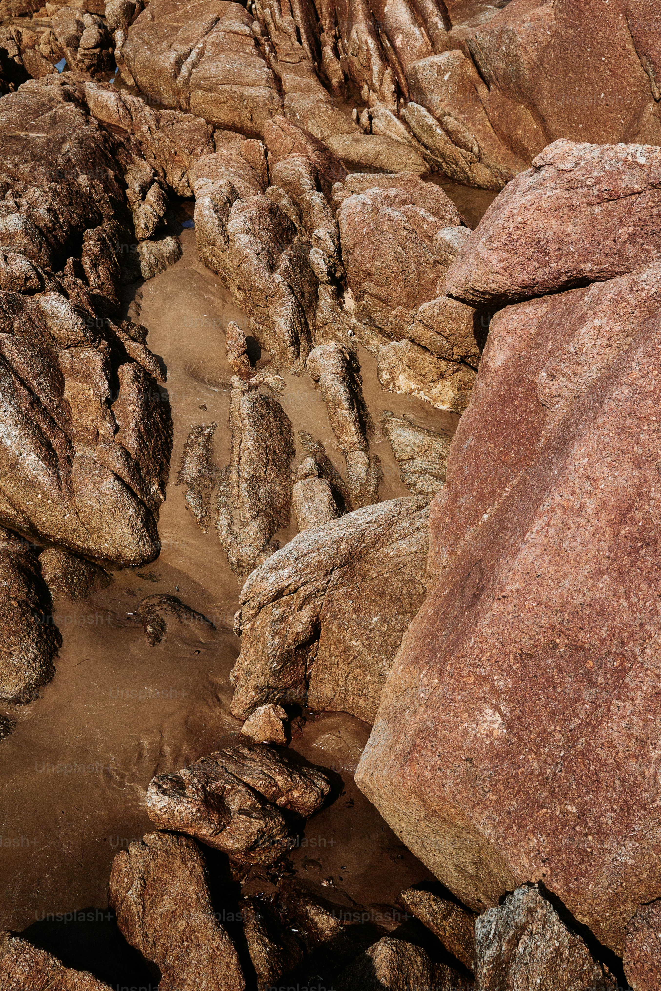 Bebatuan besar berwarna coklat kemerahan dan pasir di garis pantai yang cerah.
