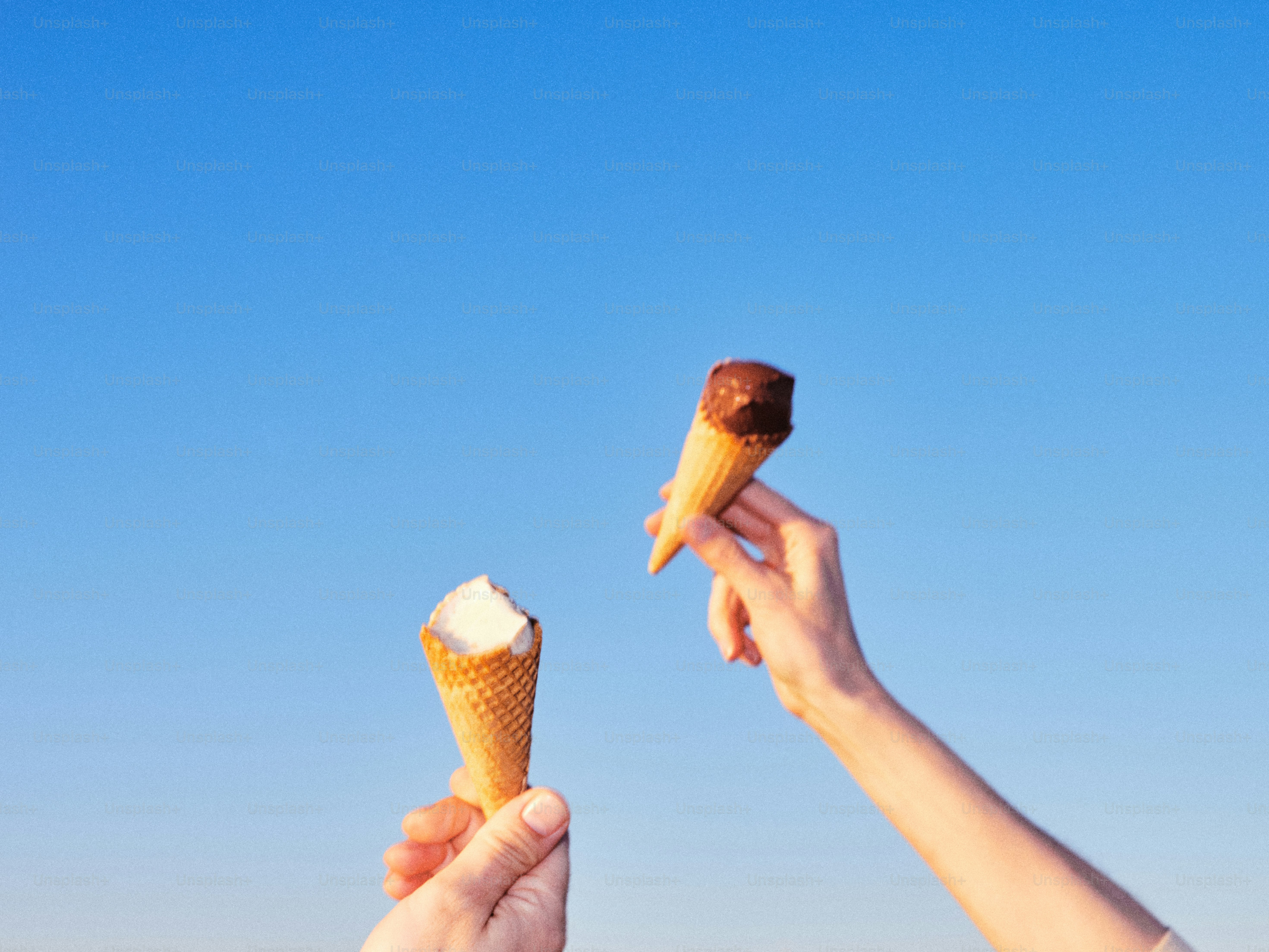 Tangan memegang dua kerucut es krim di langit biru.