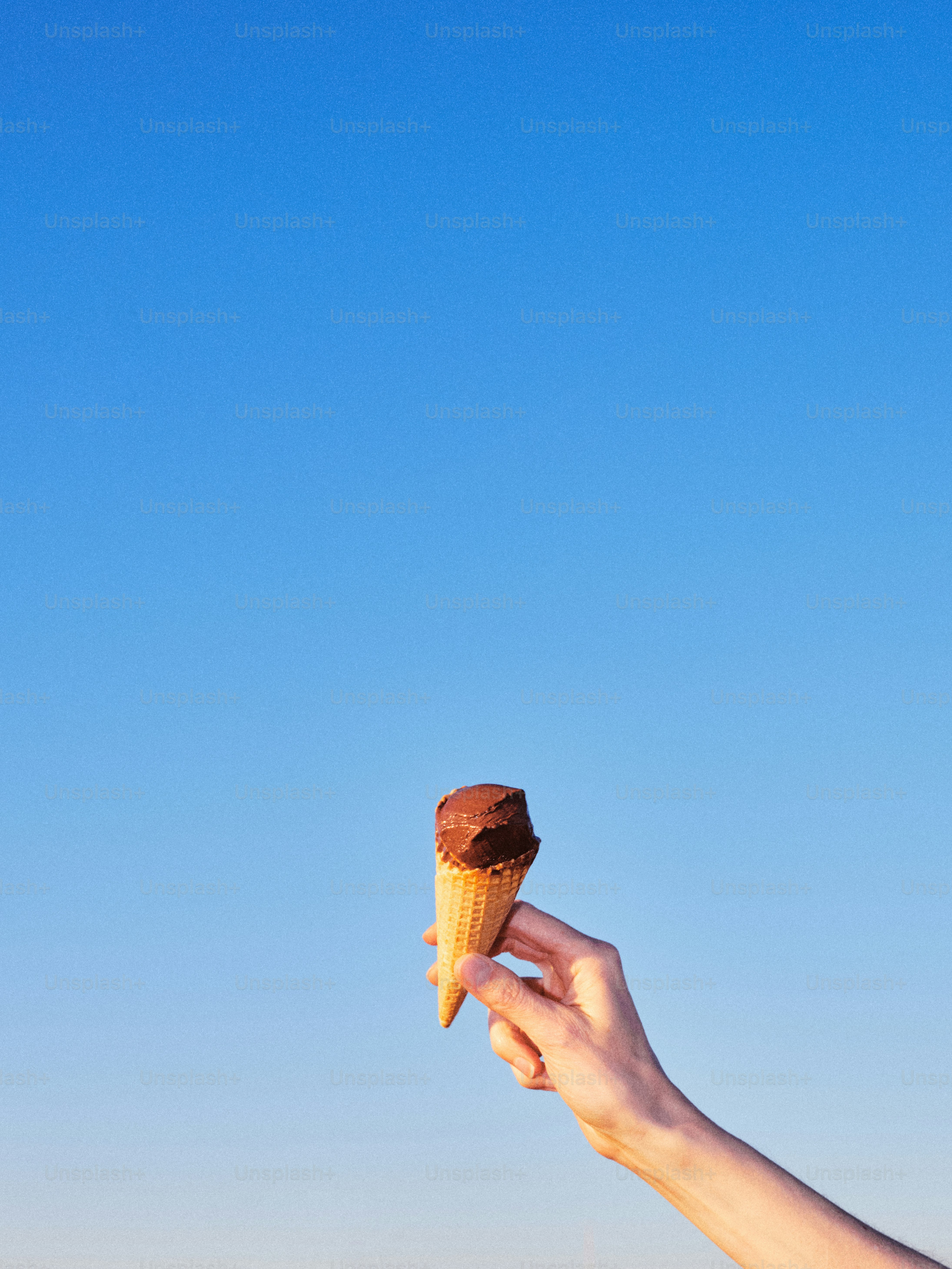 Tangan memegang kerucut es krim cokelat di bawah langit biru