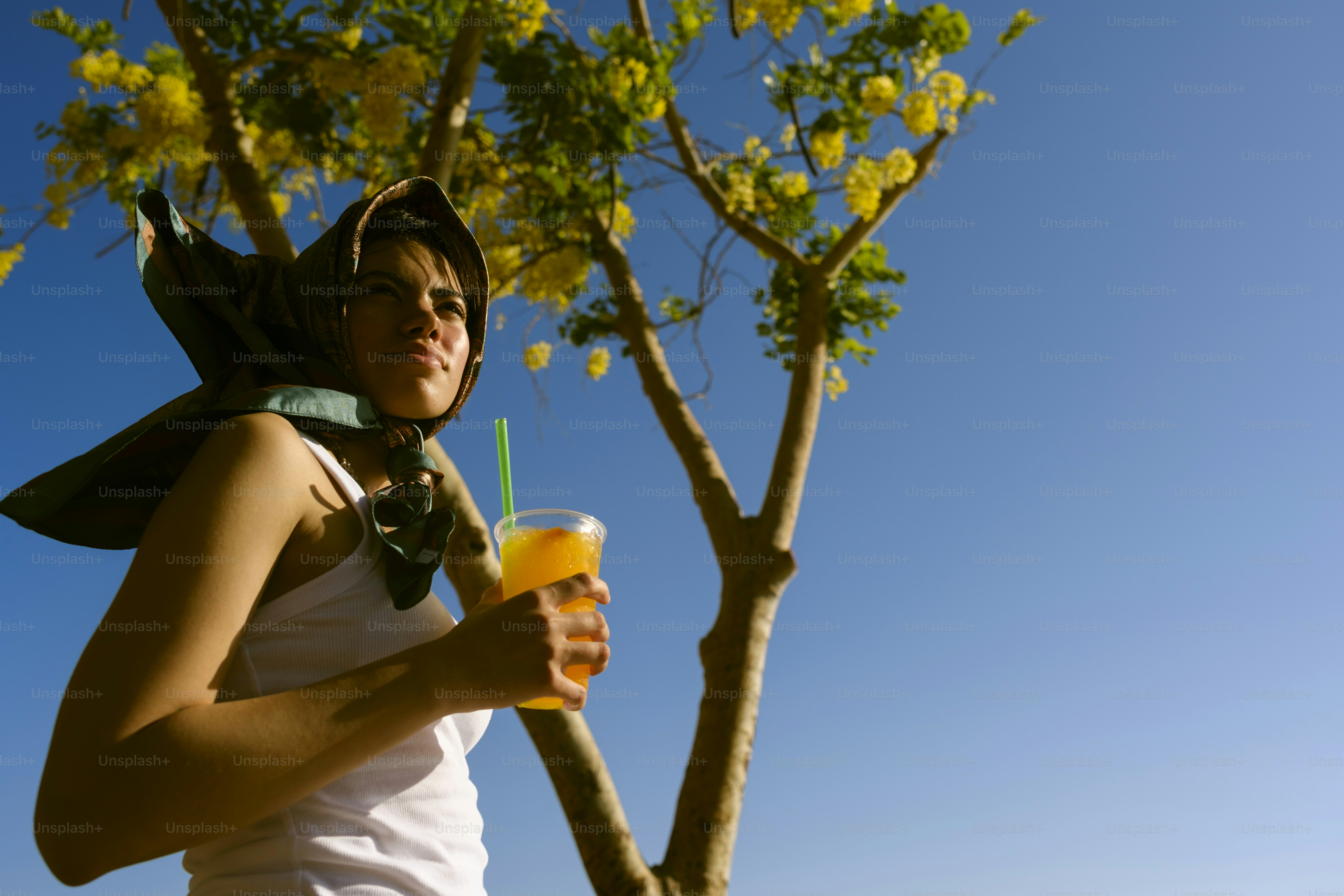 Young woman holding a drink under a flowering tree.