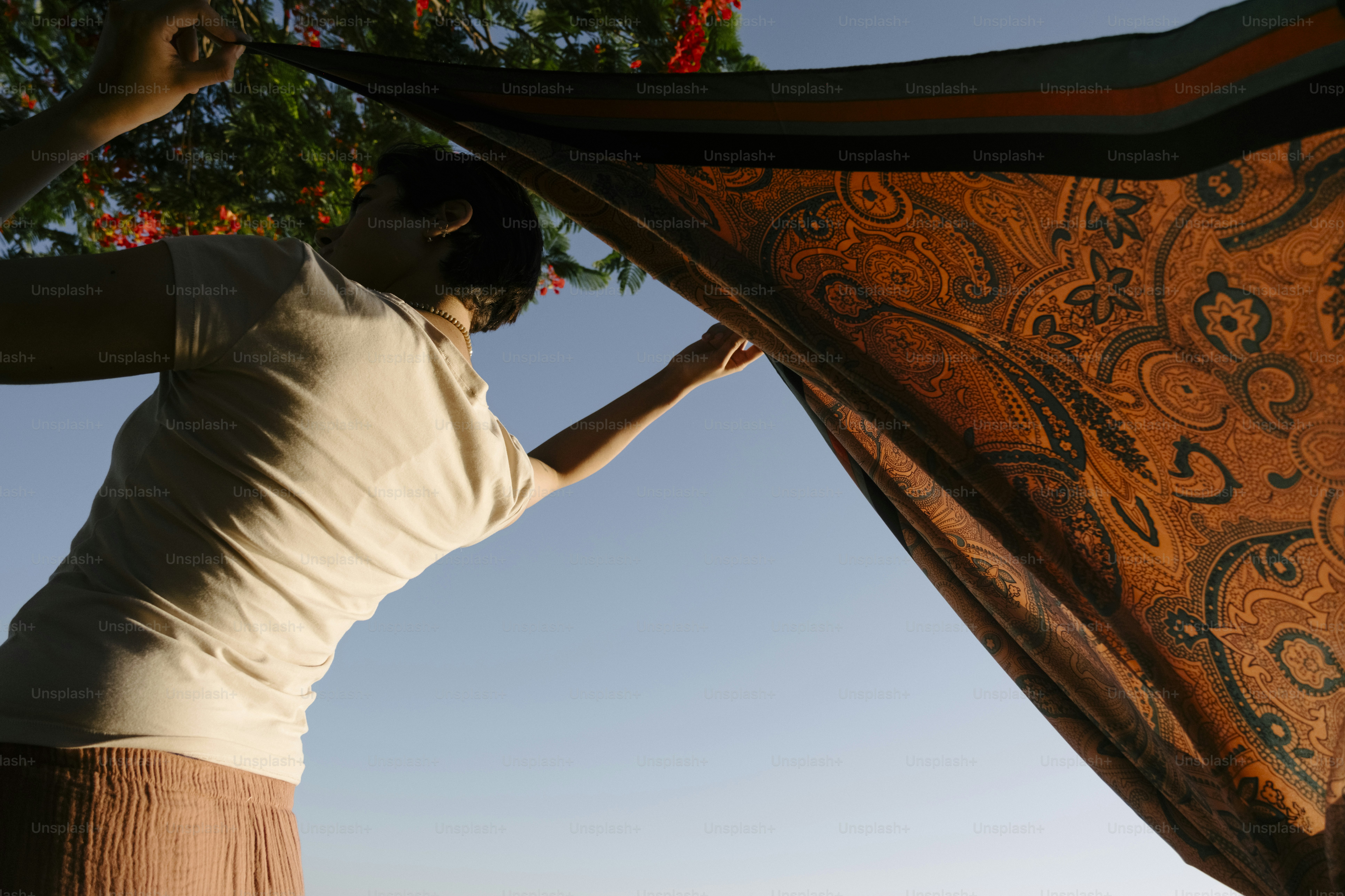 Woman holding up an orange paisley fabric against blue sky