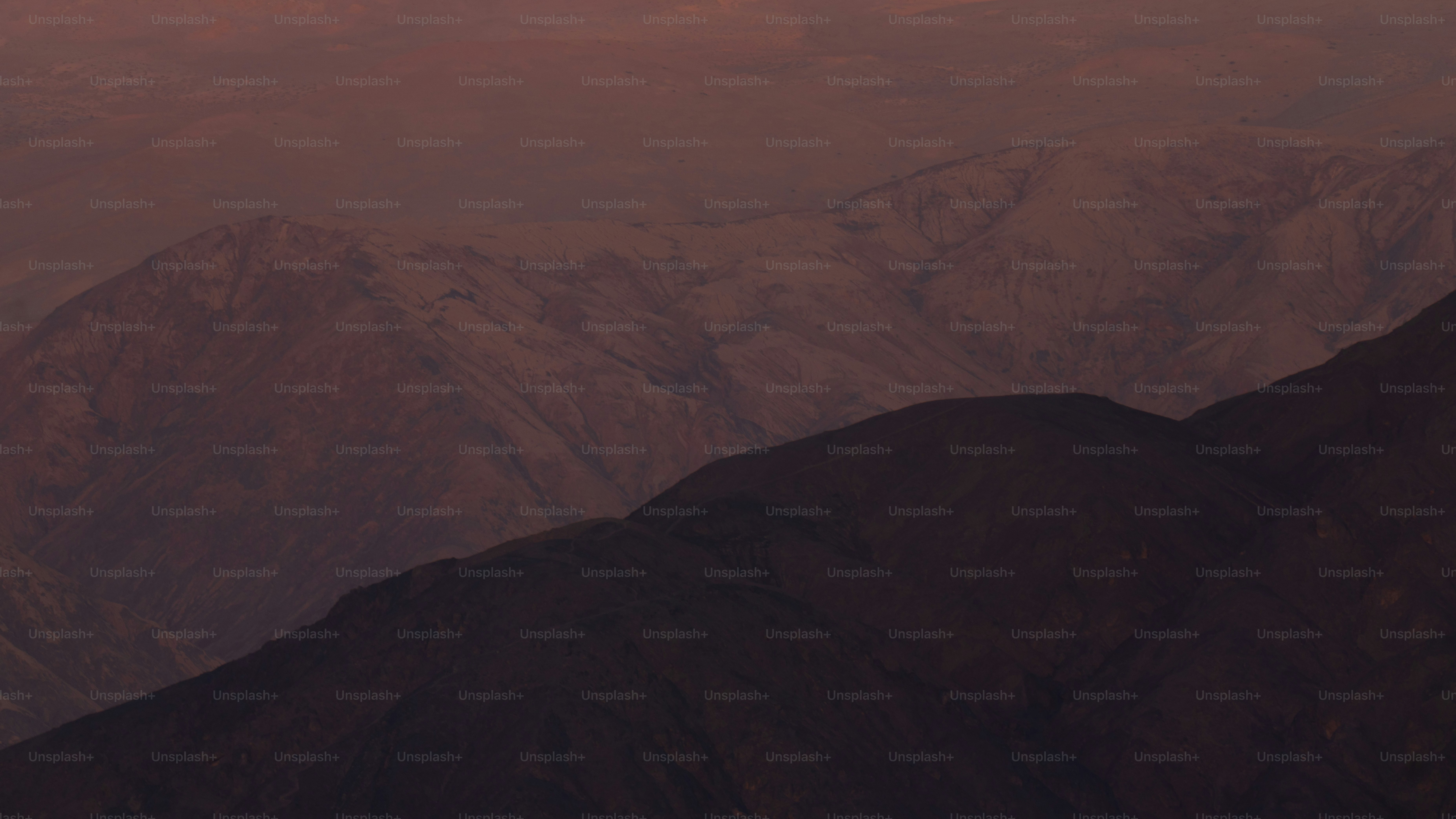 Capas de montañas bajo un cielo rojizo y brumoso al atardecer.