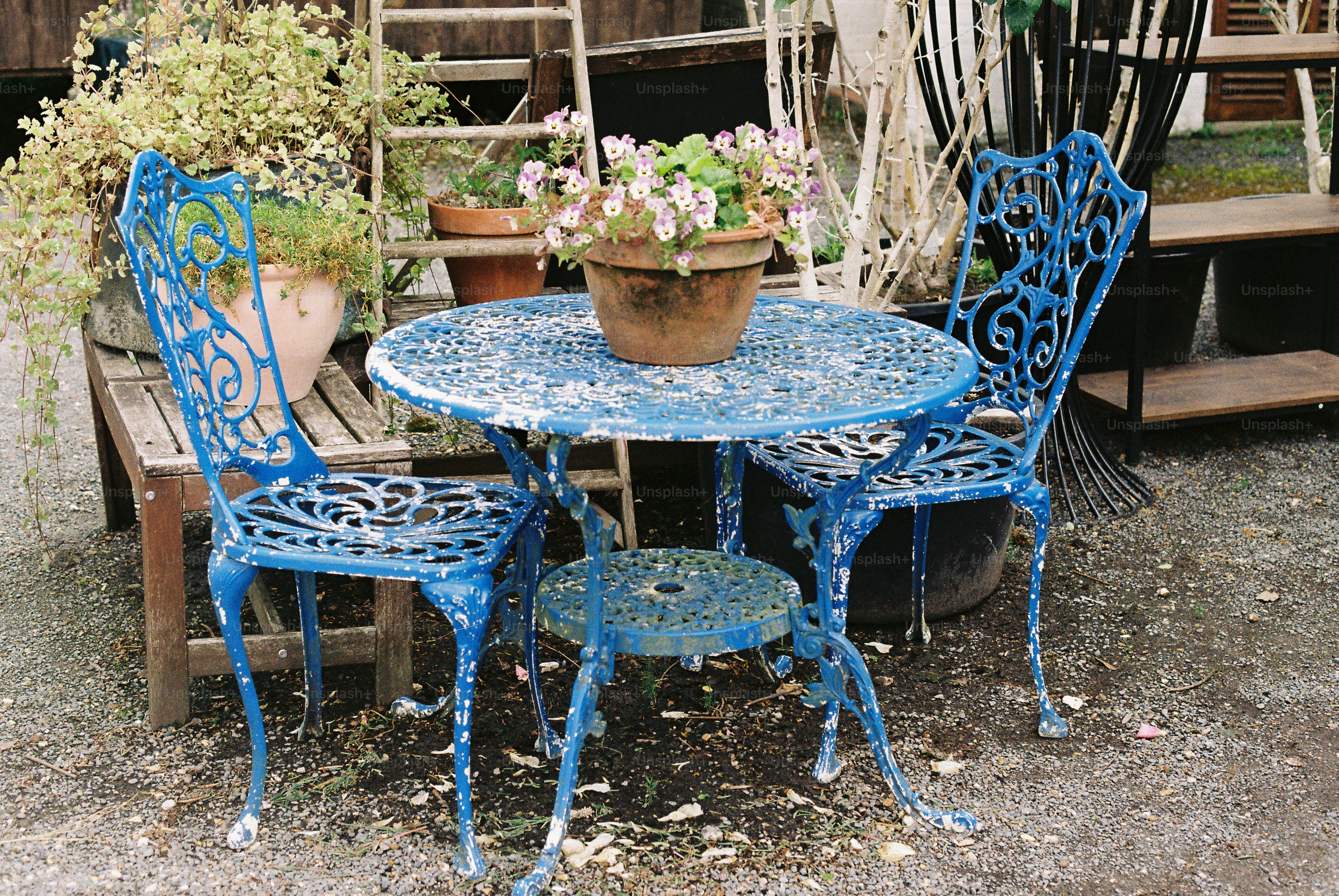 Furnitur taman biru lapuk berornamen dengan bunga pot