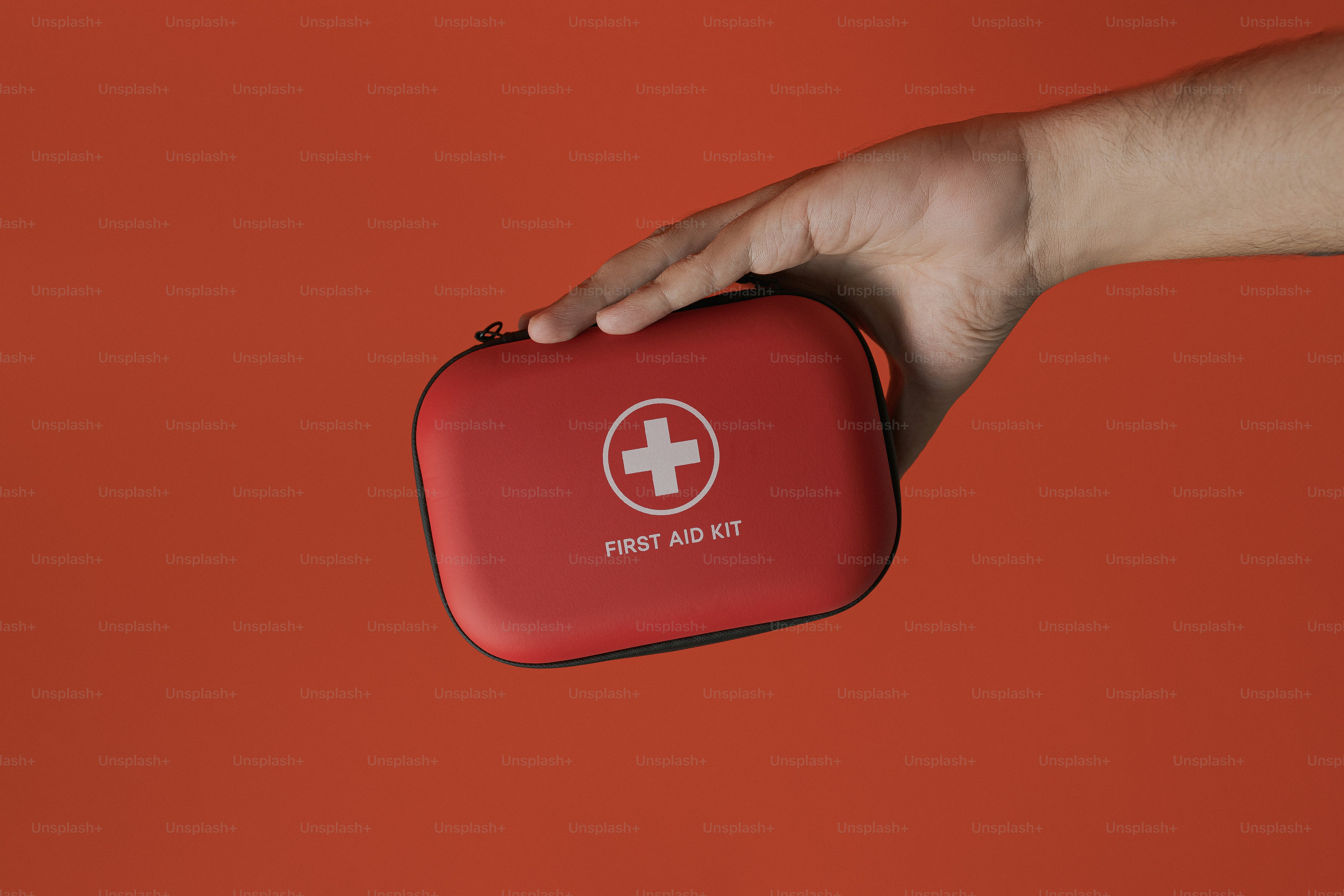 Handhaltend roter Erste-Hilfe-Kasten vor orangefarbenem Hintergrund