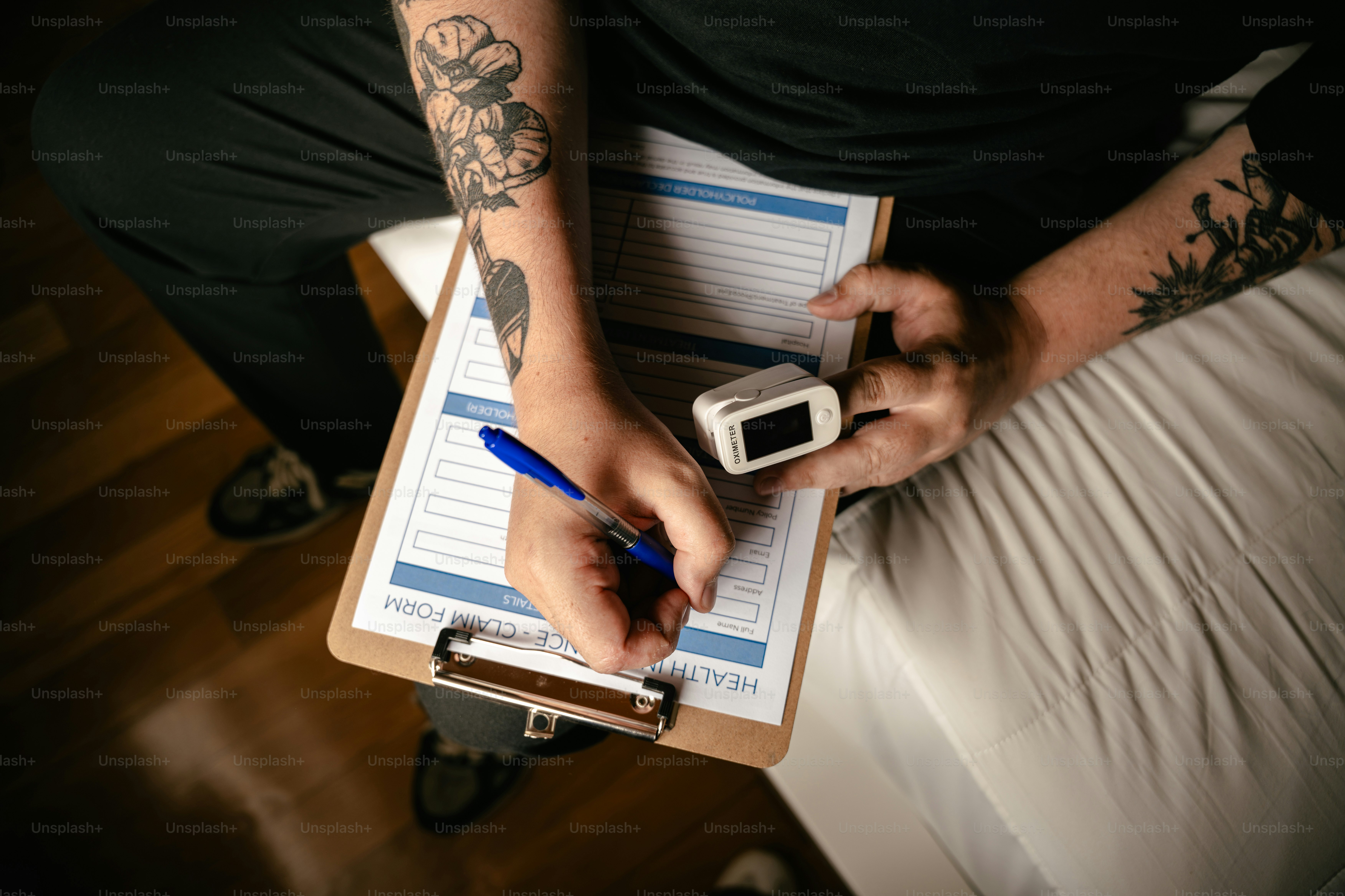 Tattooed hands writing on a clipboard, holding pulse oximeter