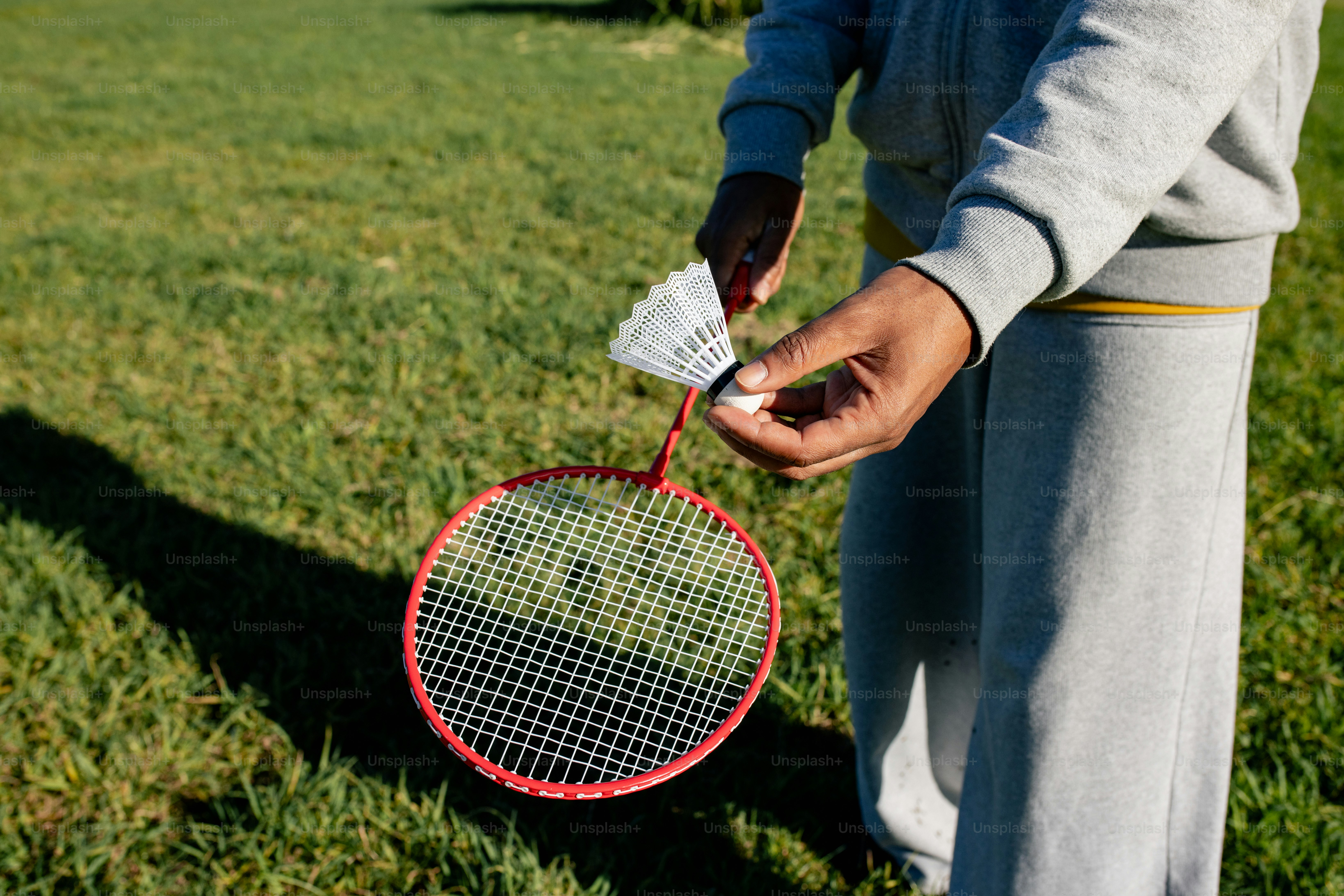 Hands holding badminton racket and shuttlecock on grass