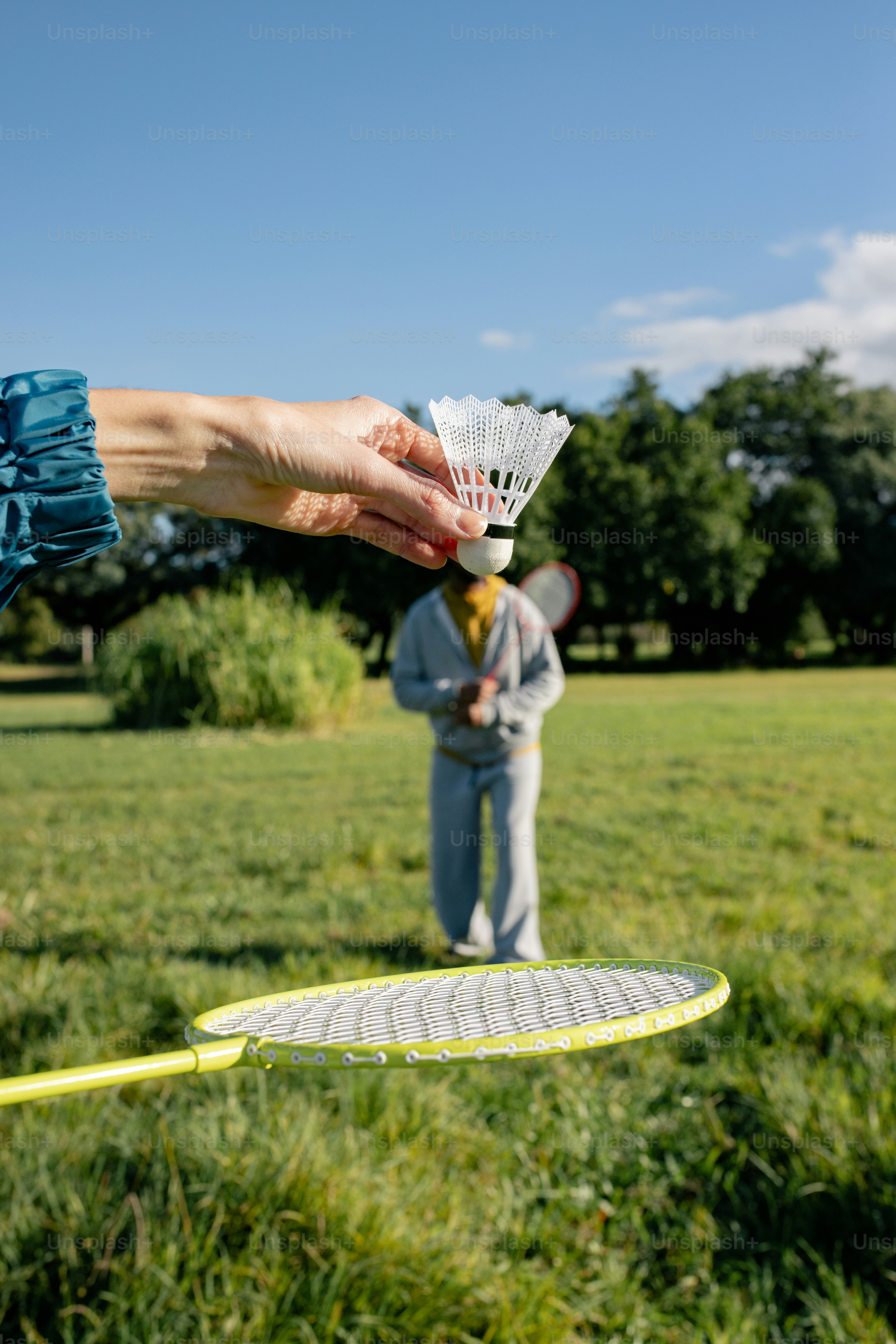 Hand holding shuttlecock above badminton racket outdoors