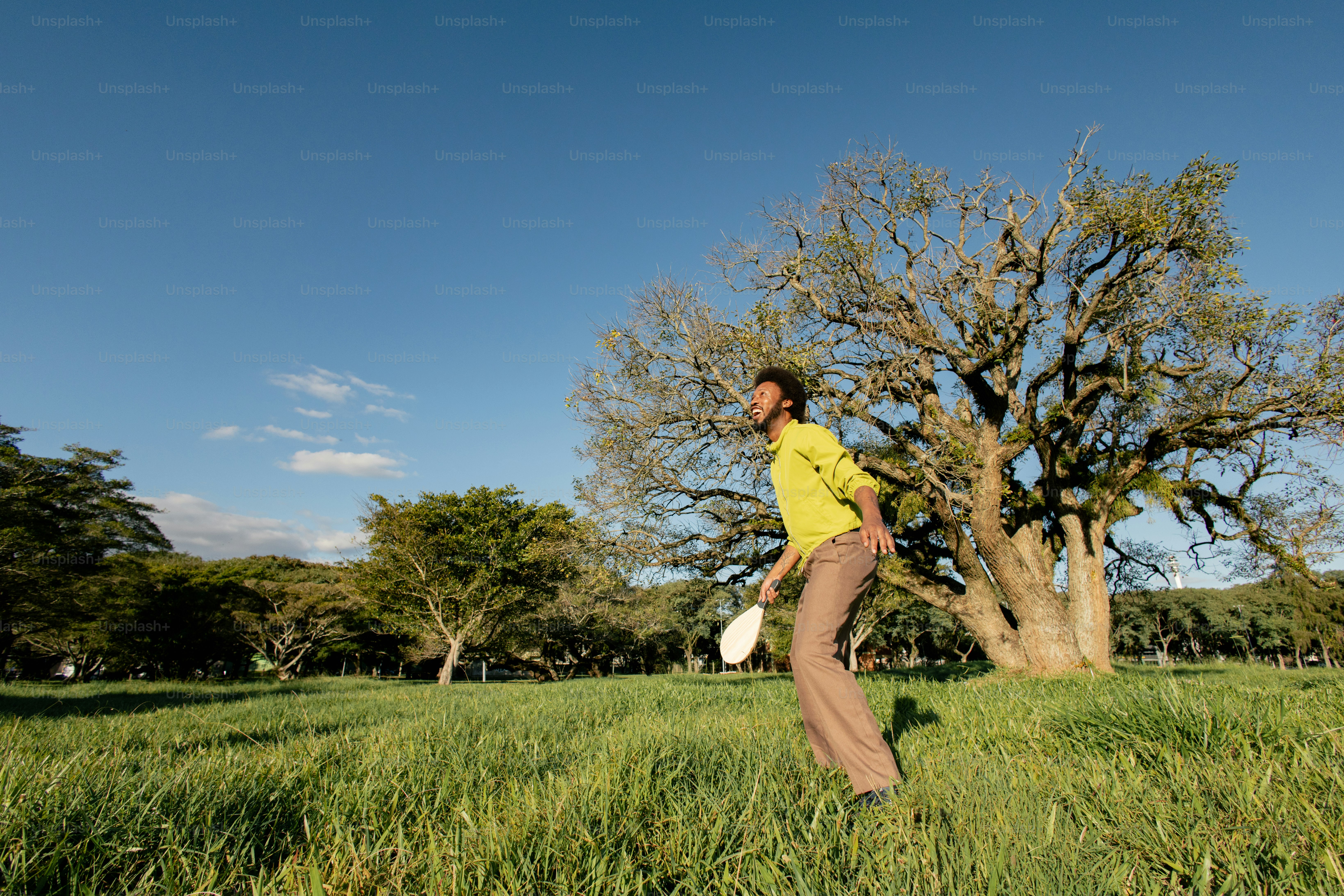 Man playing with racket in grassy field, large tree