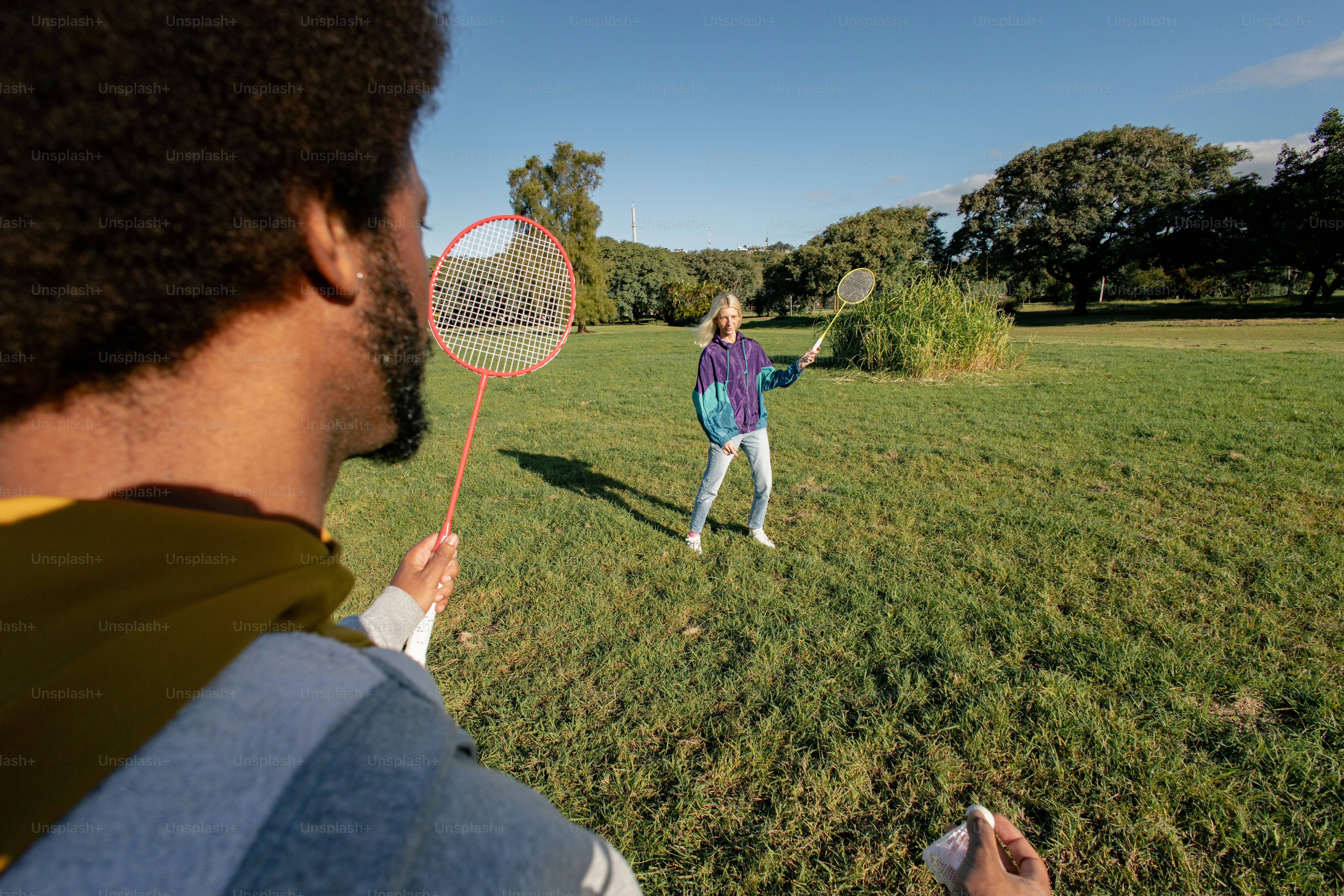Two people playing badminton in a sunny park