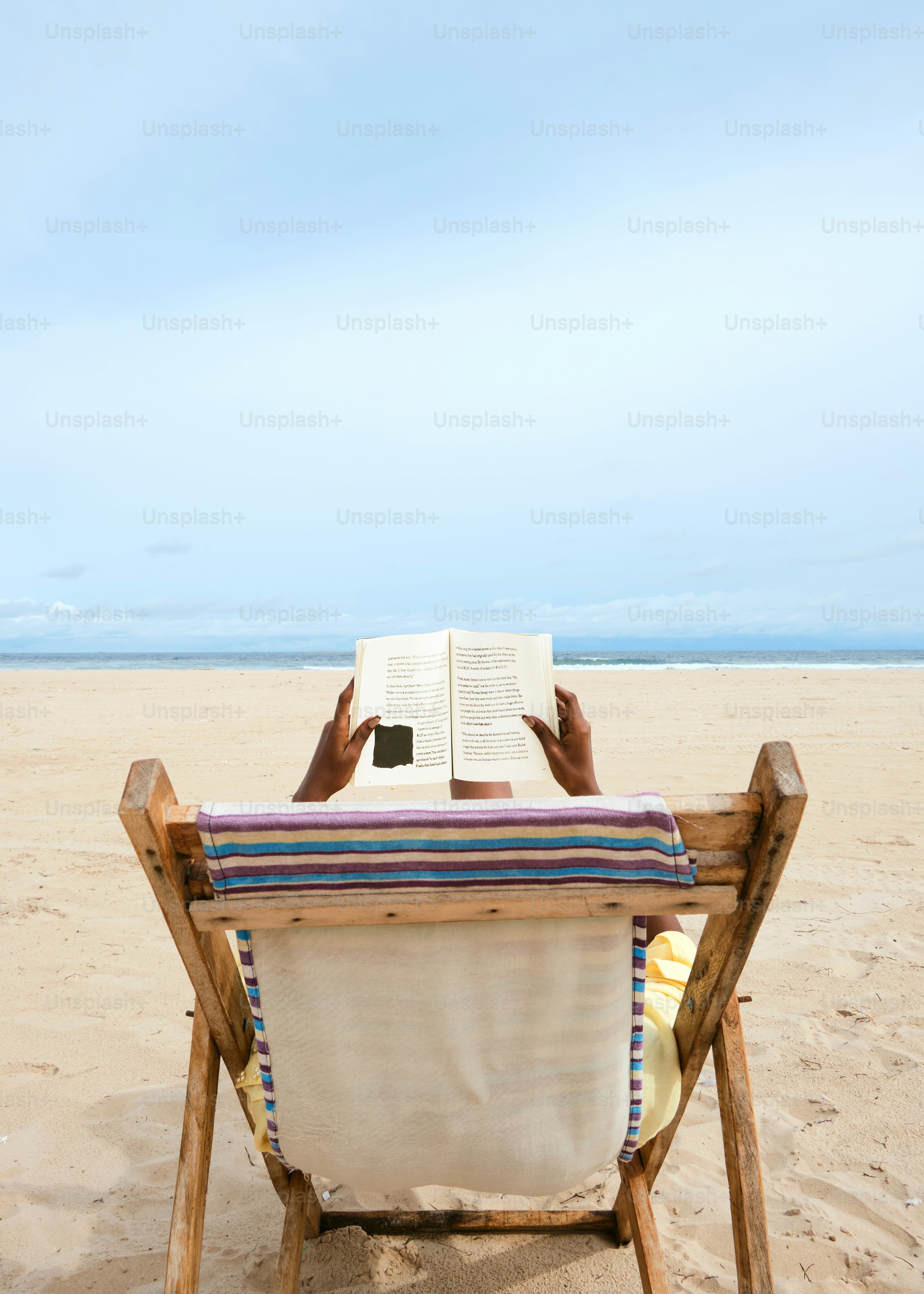 砂浜の上でビーチチェアに座って本を読む人