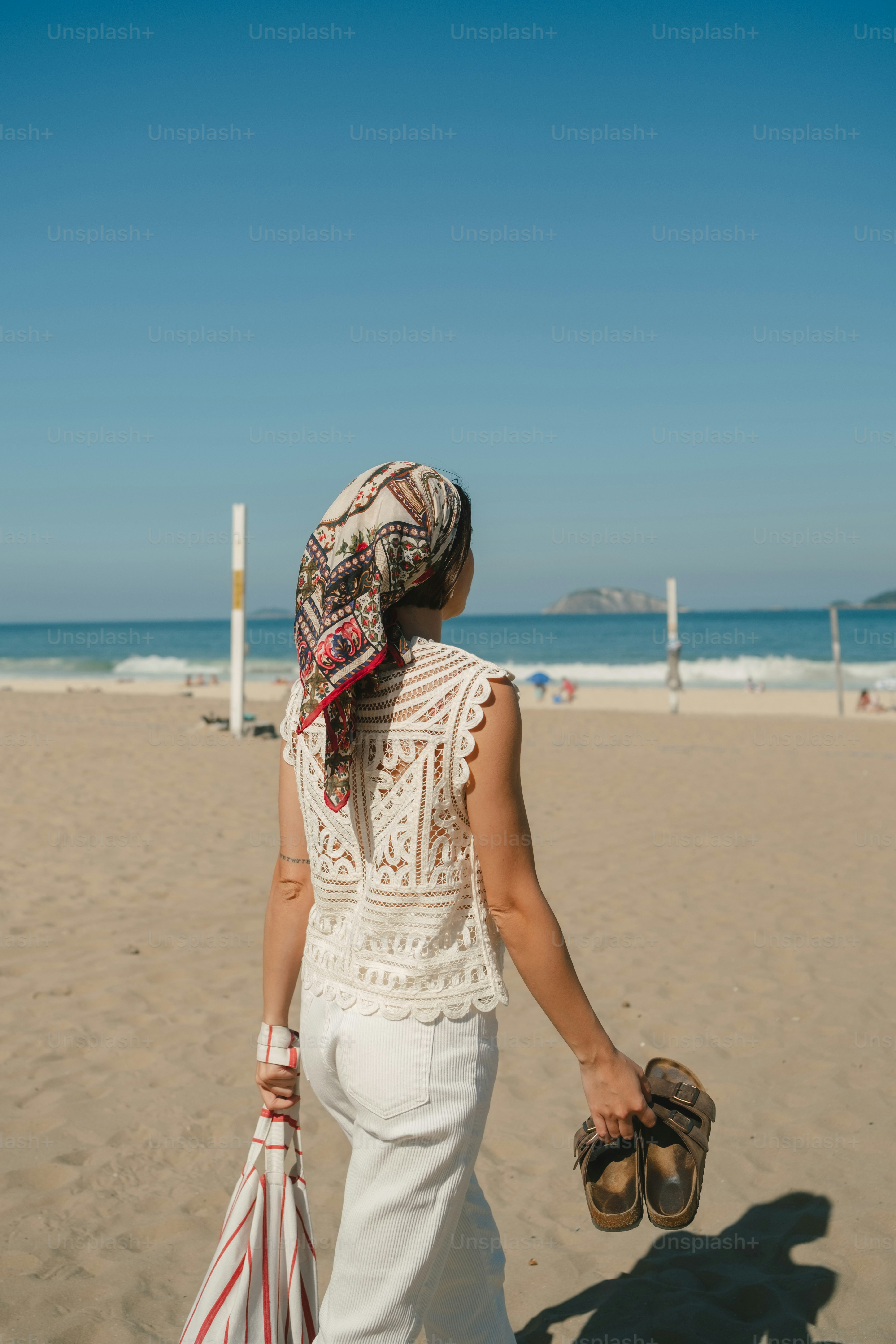 Woman in headscarf walks on sandy beach by ocean