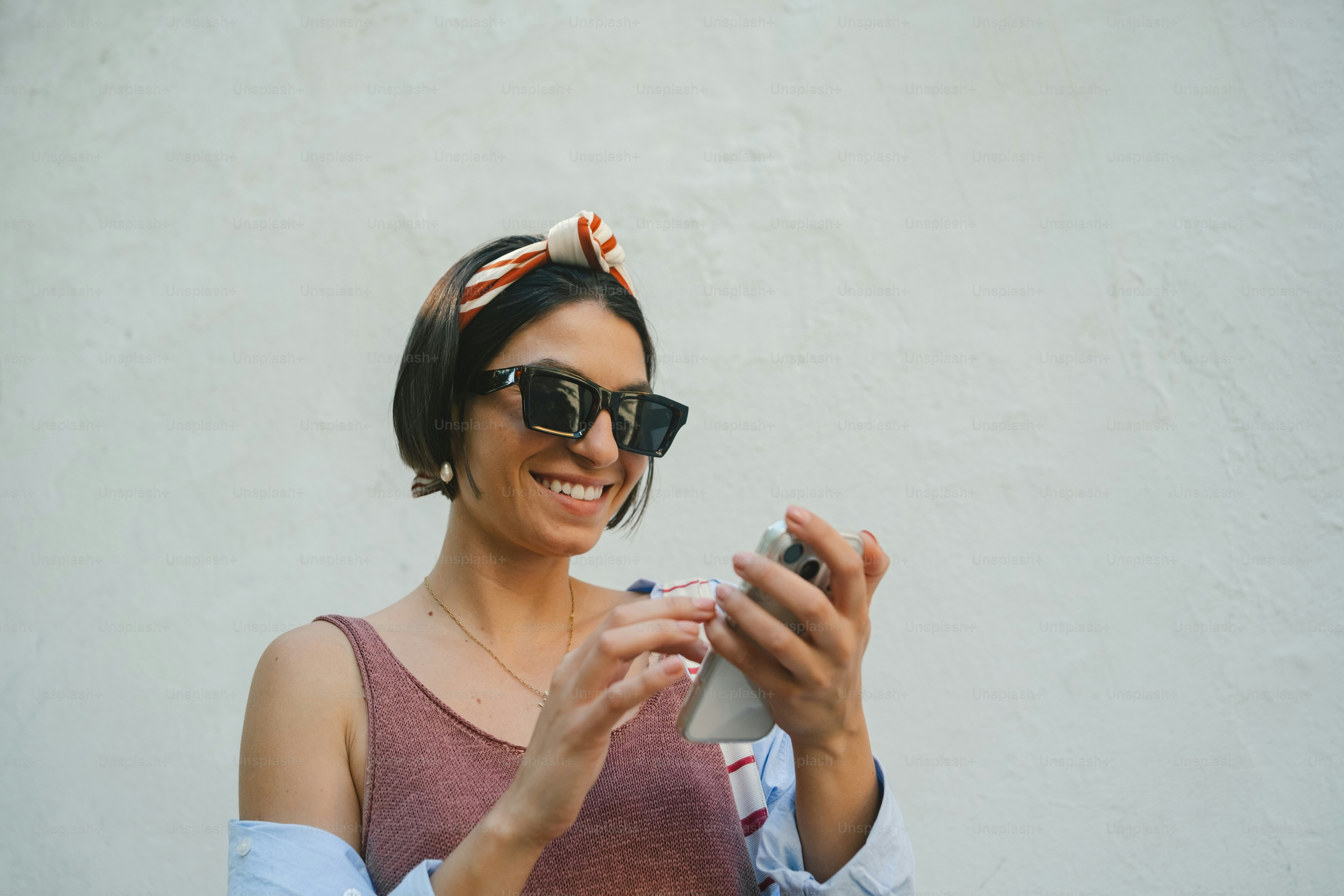 Smiling woman in sunglasses and headband using smartphone