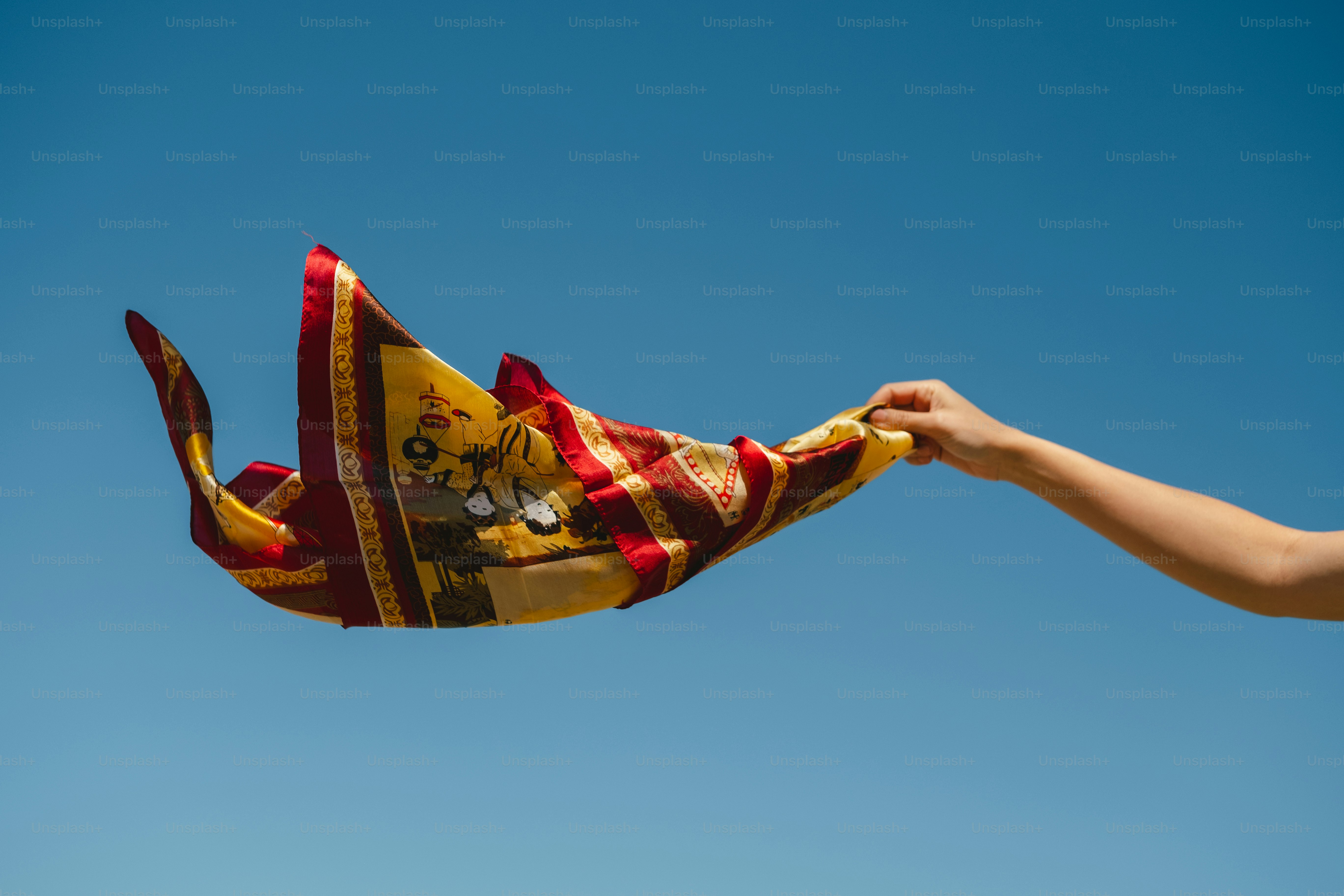 Hand holding colorful patterned scarf against blue sky
