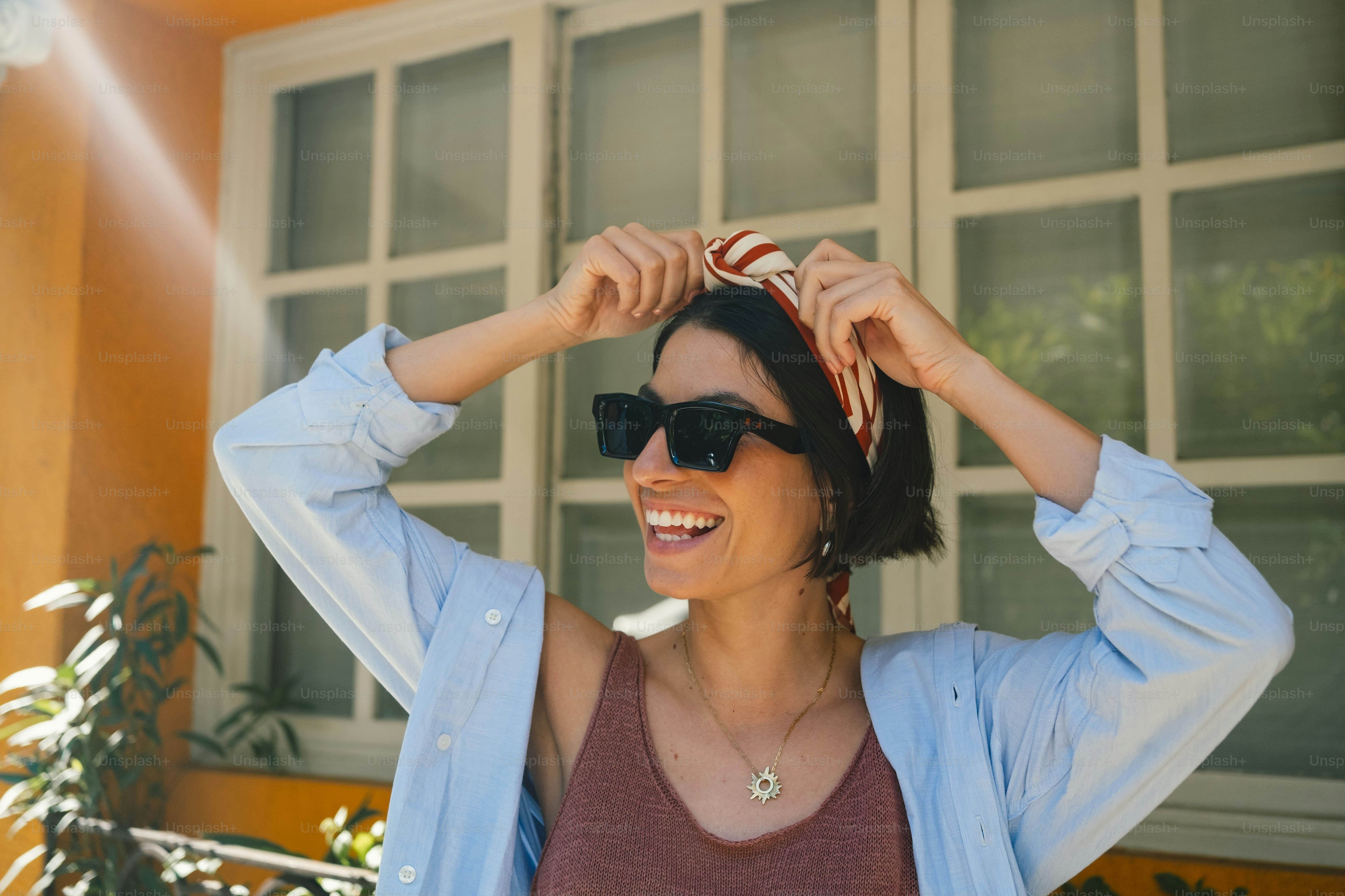 Smiling woman adjusting headscarf and sunglasses in sunlight