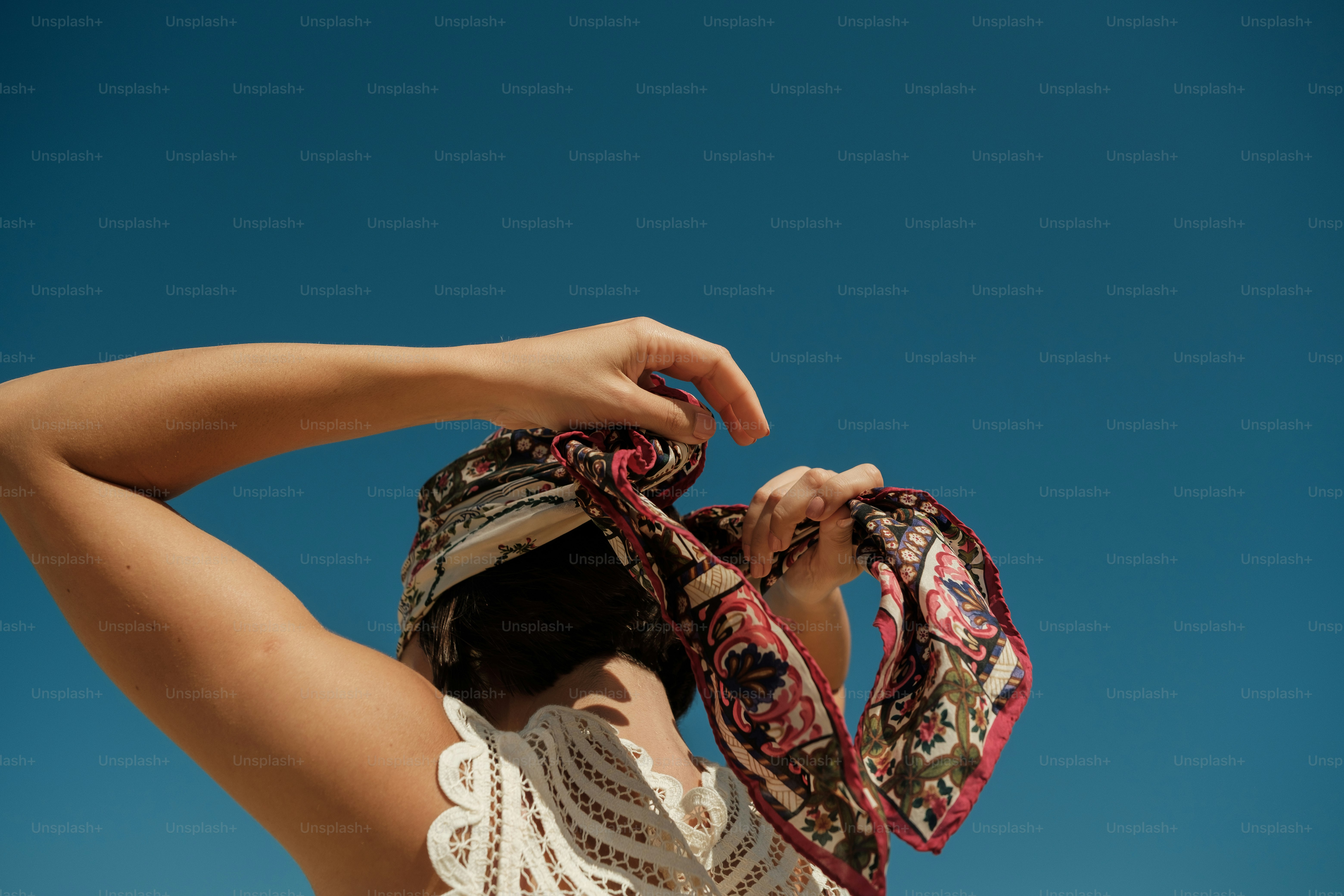 Woman tying patterned headscarf against blue sky