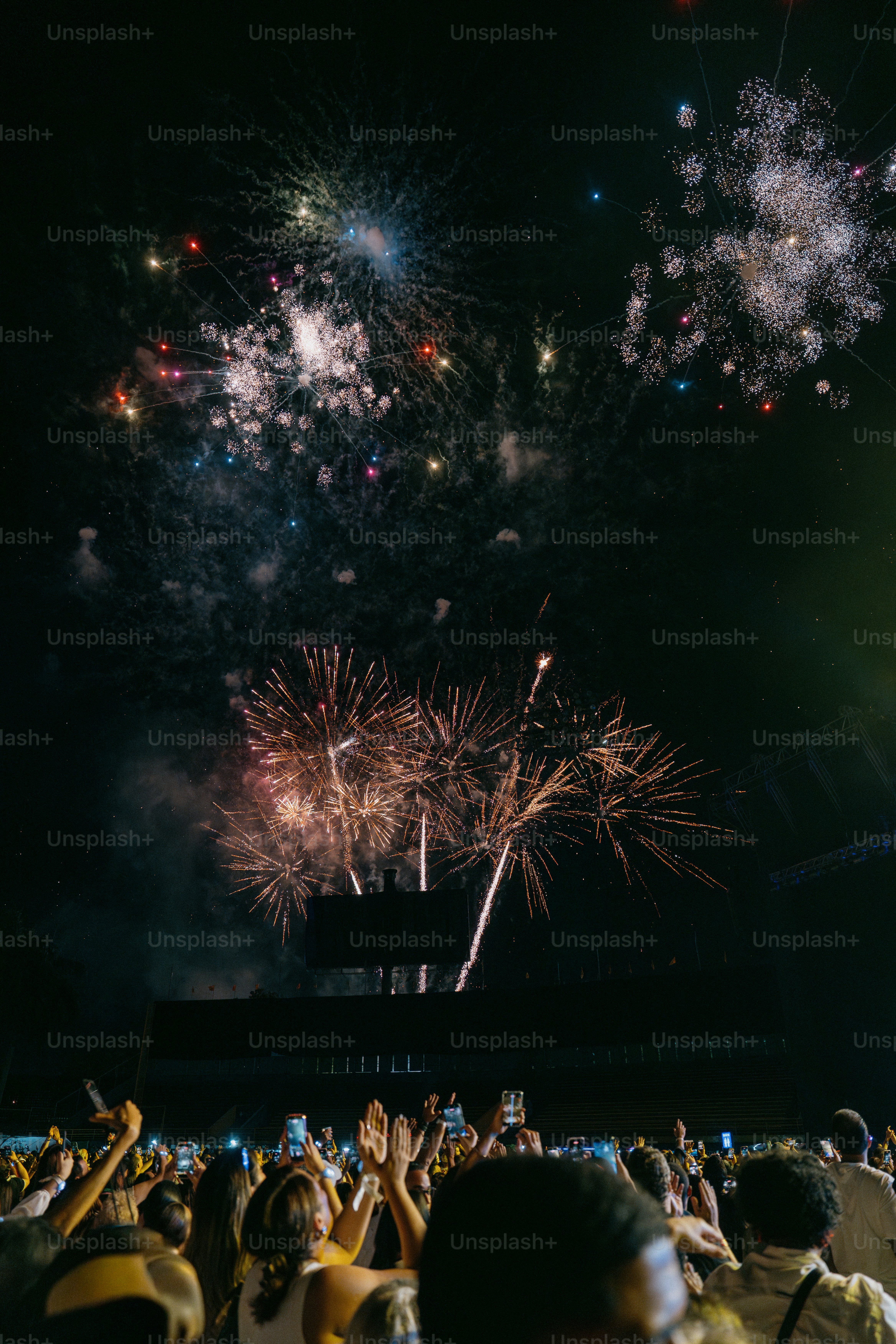 Multidão assistindo fogos de artifício coloridos iluminando o céu noturno