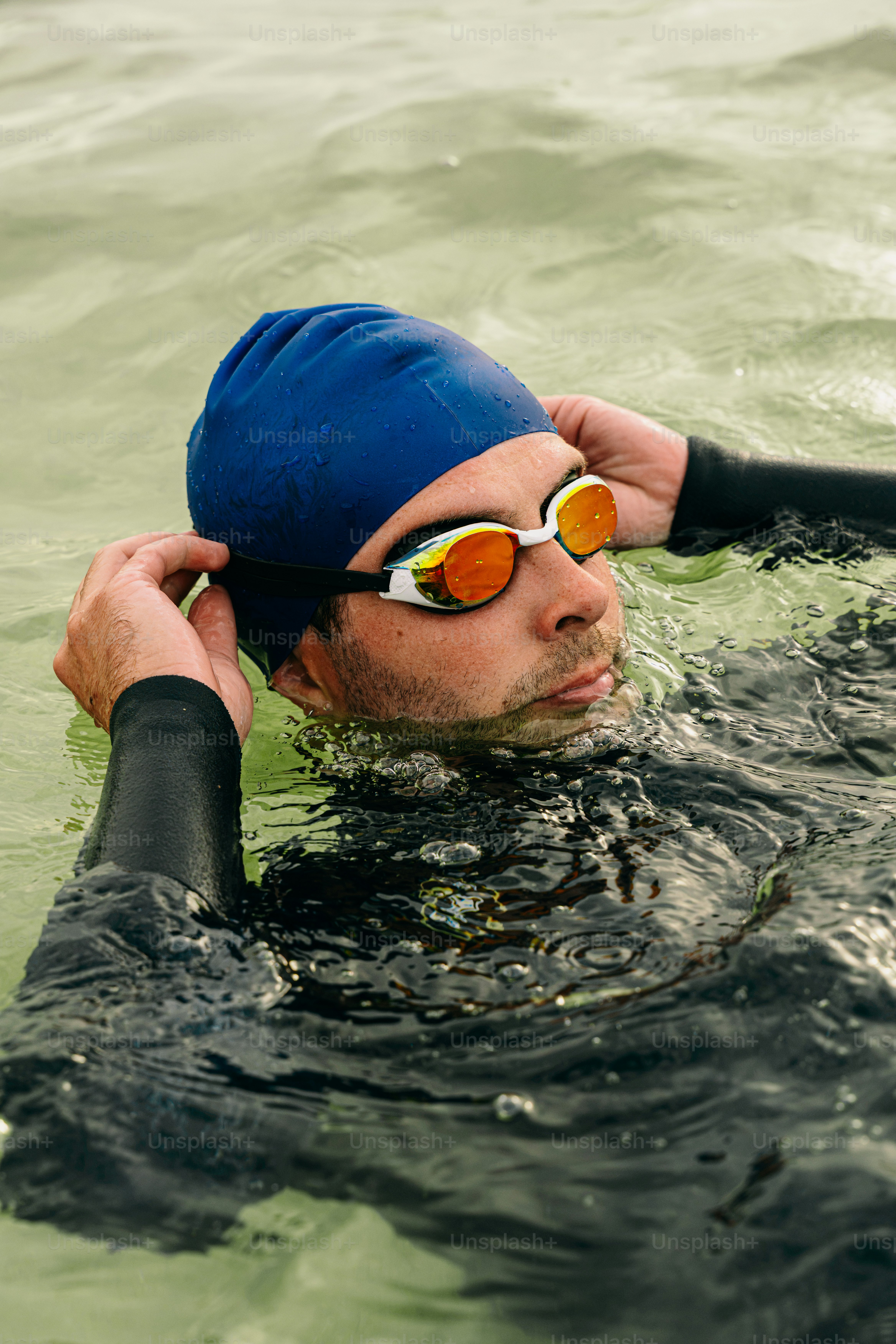 Swimmer in wetsuit adjusting blue swim cap and goggles