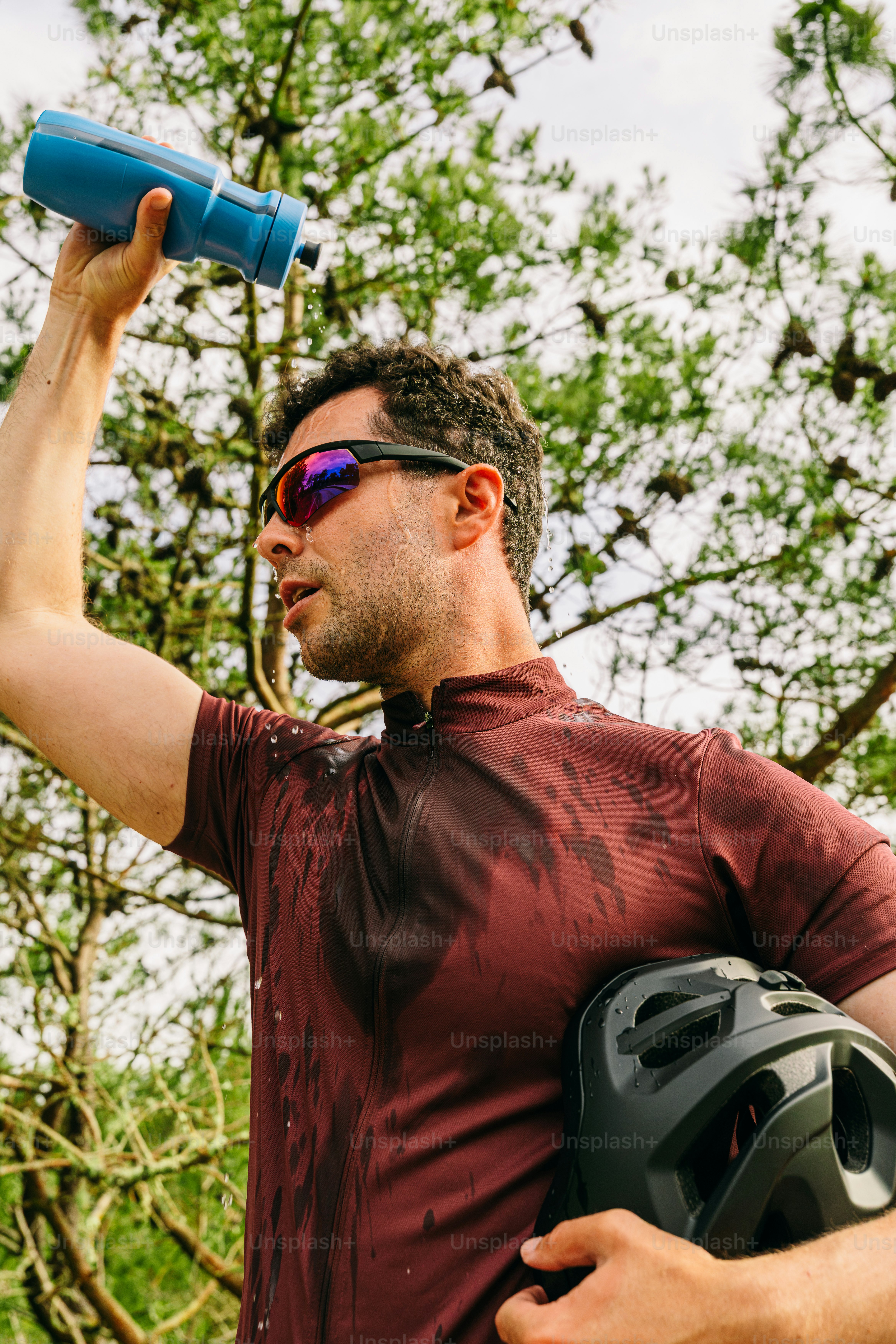 Cyclist pouring water on head, holding helmet