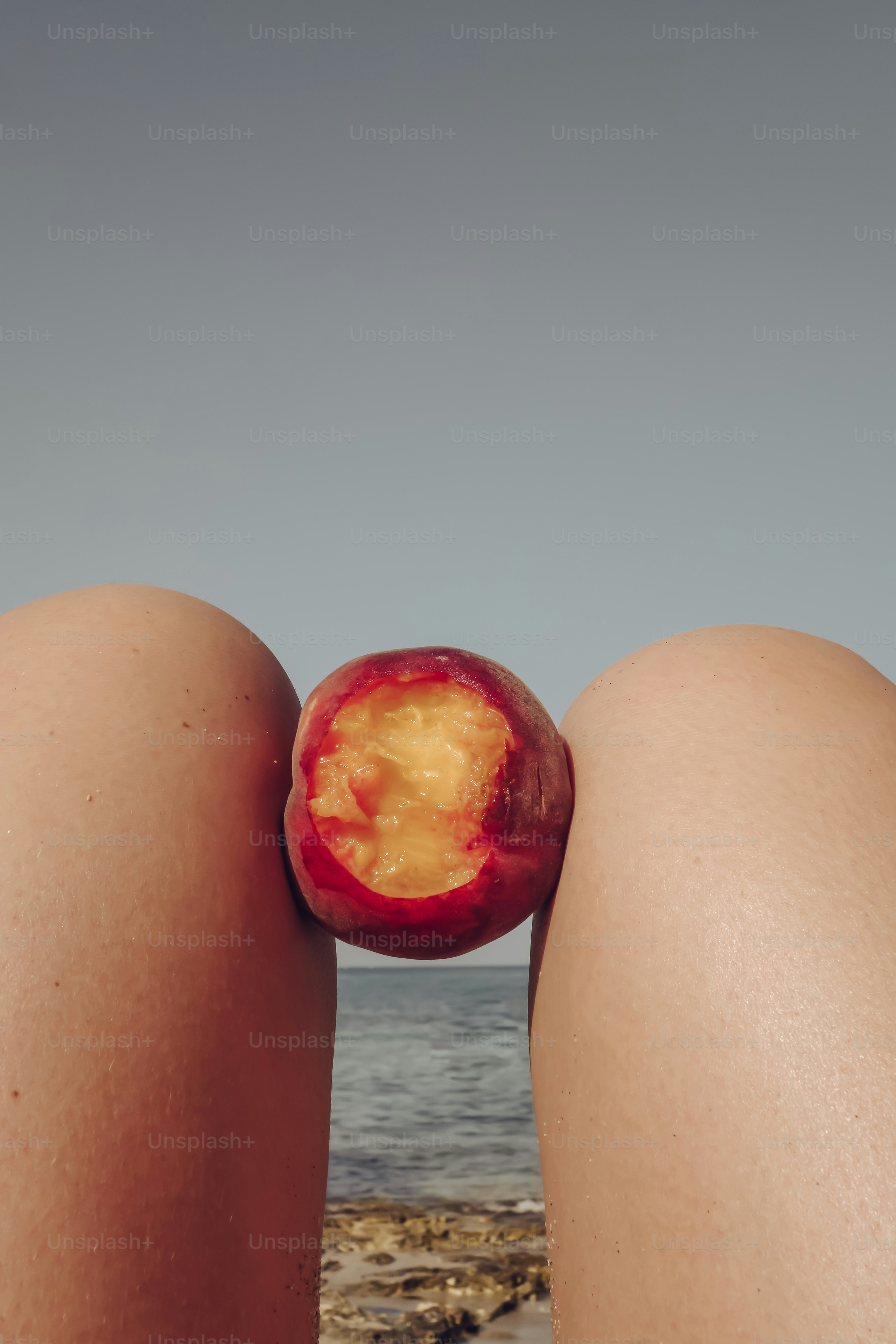 Partially eaten peach between knees by the ocean