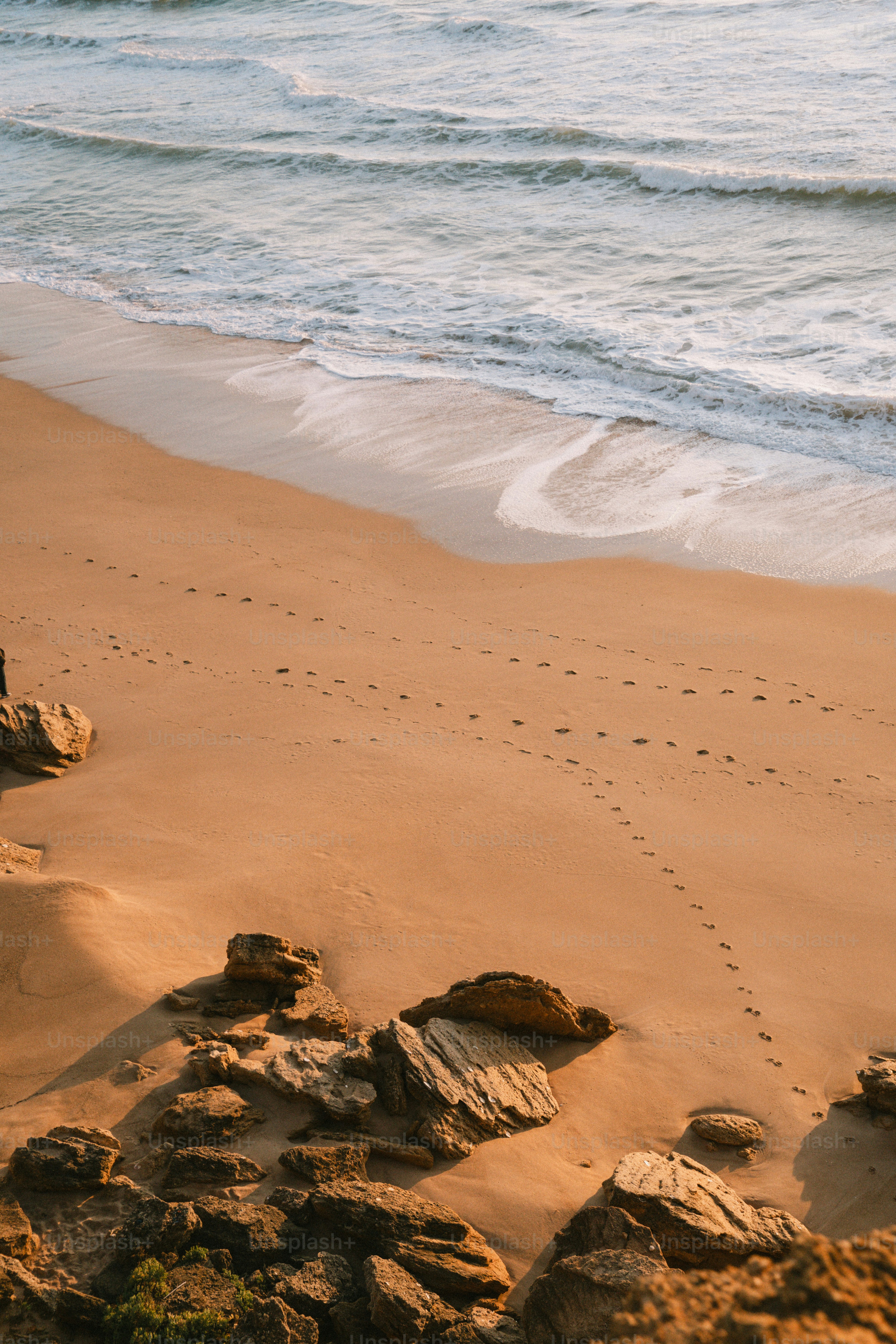 Wellen, die mit Steinen an den Sandstrand spülen