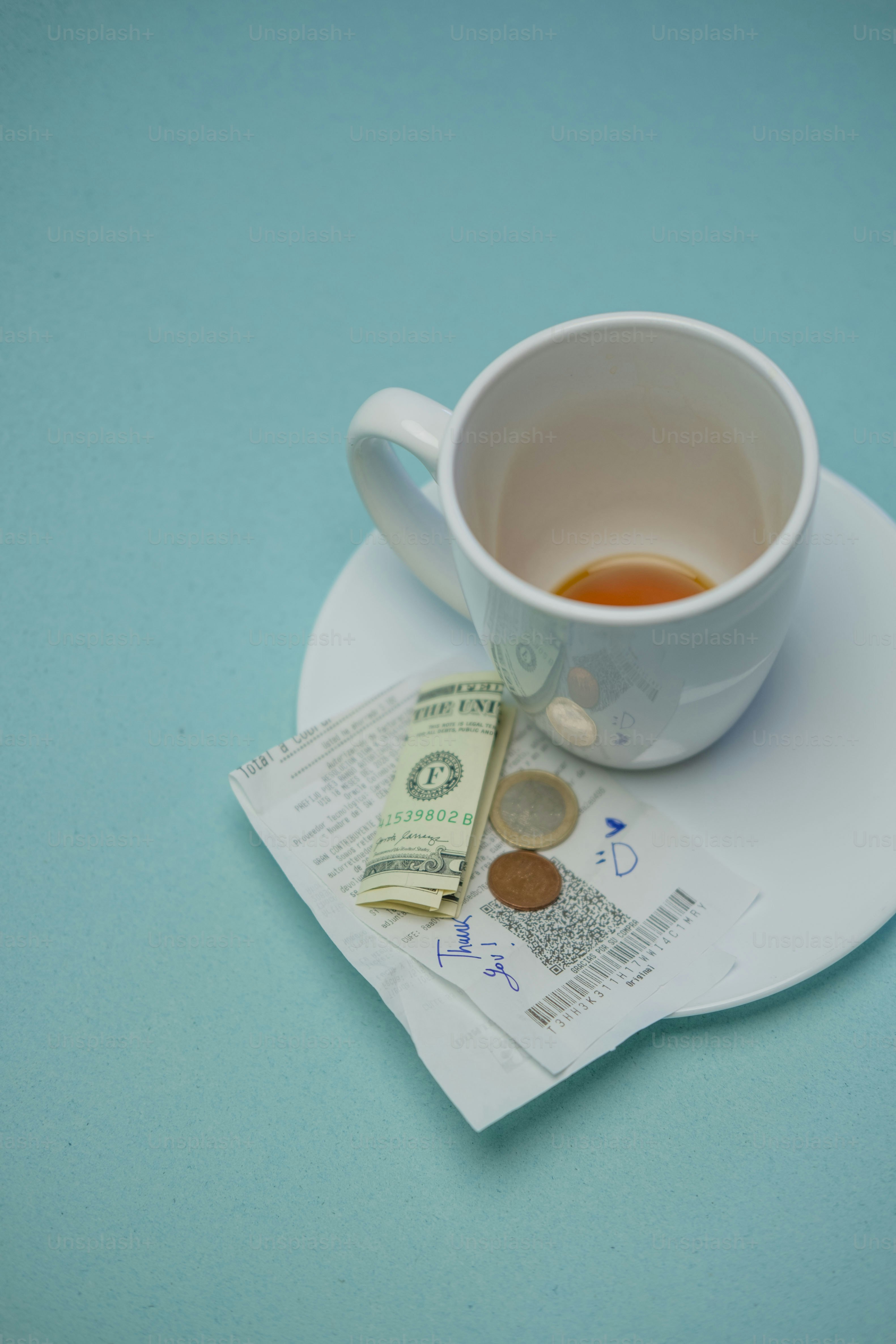 Empty coffee cup, bill, and coins on blue surface