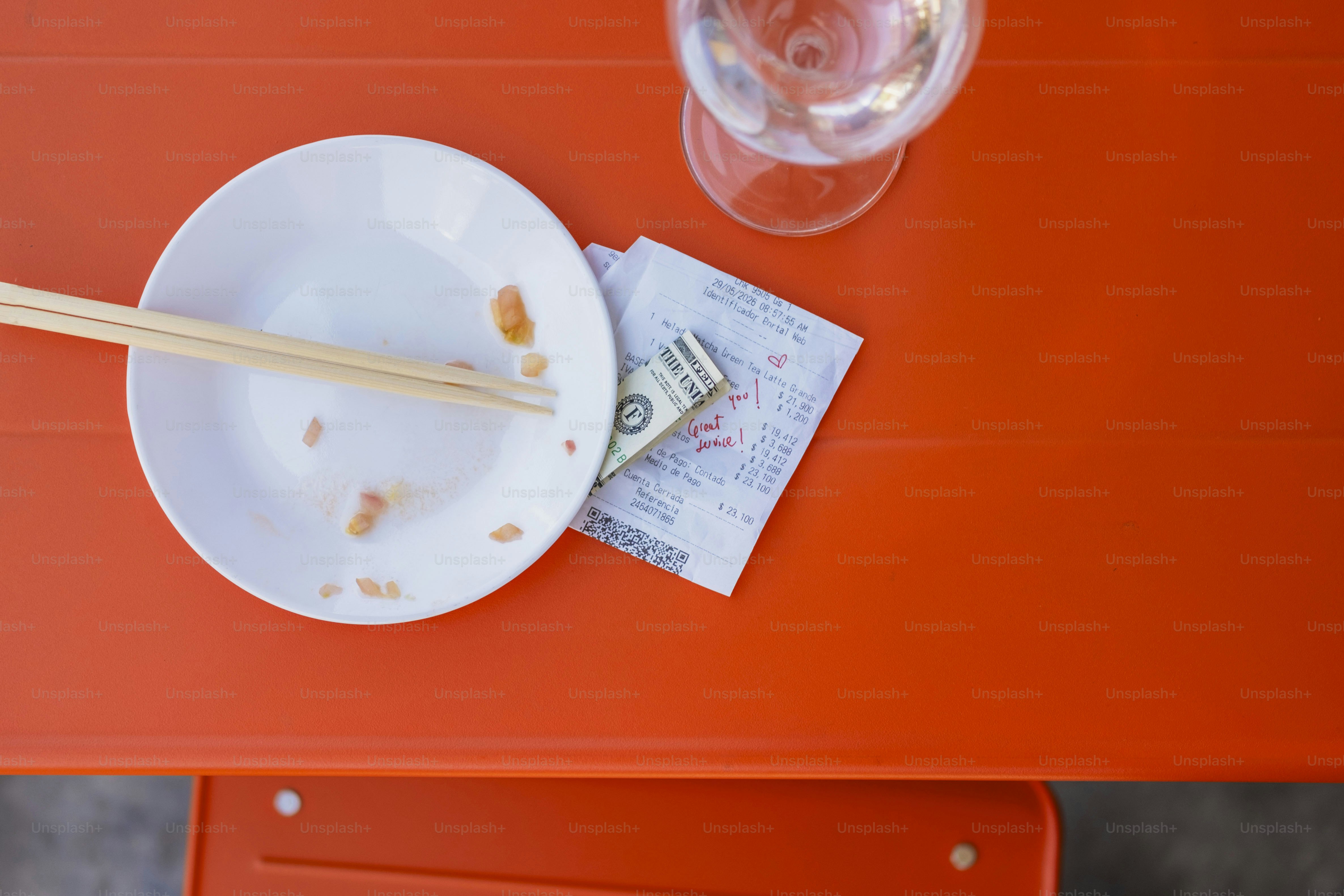 Empty plate, chopsticks, bill, wine glass on orange table