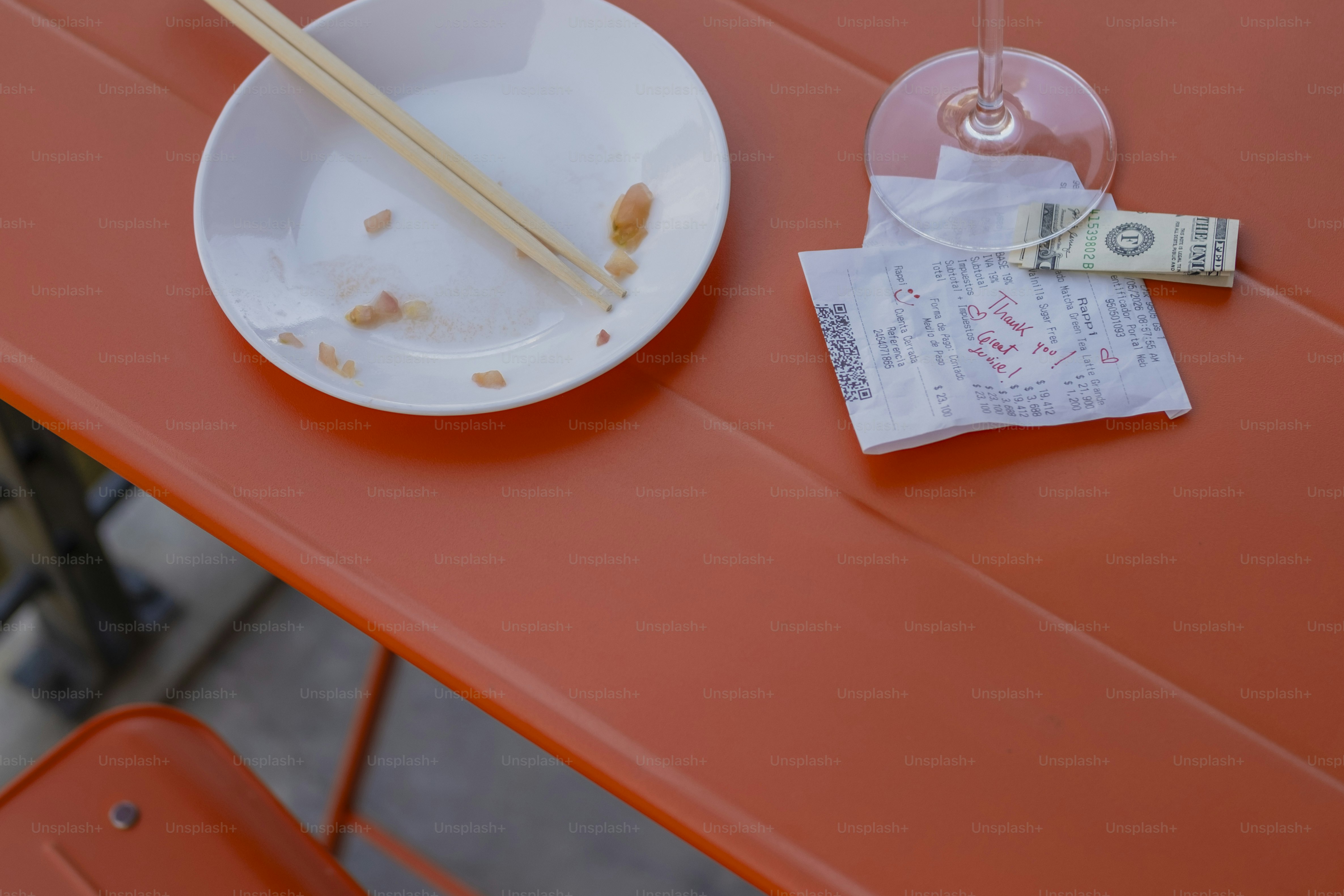 Empty plate, chopsticks, receipt, dollar bill on orange table