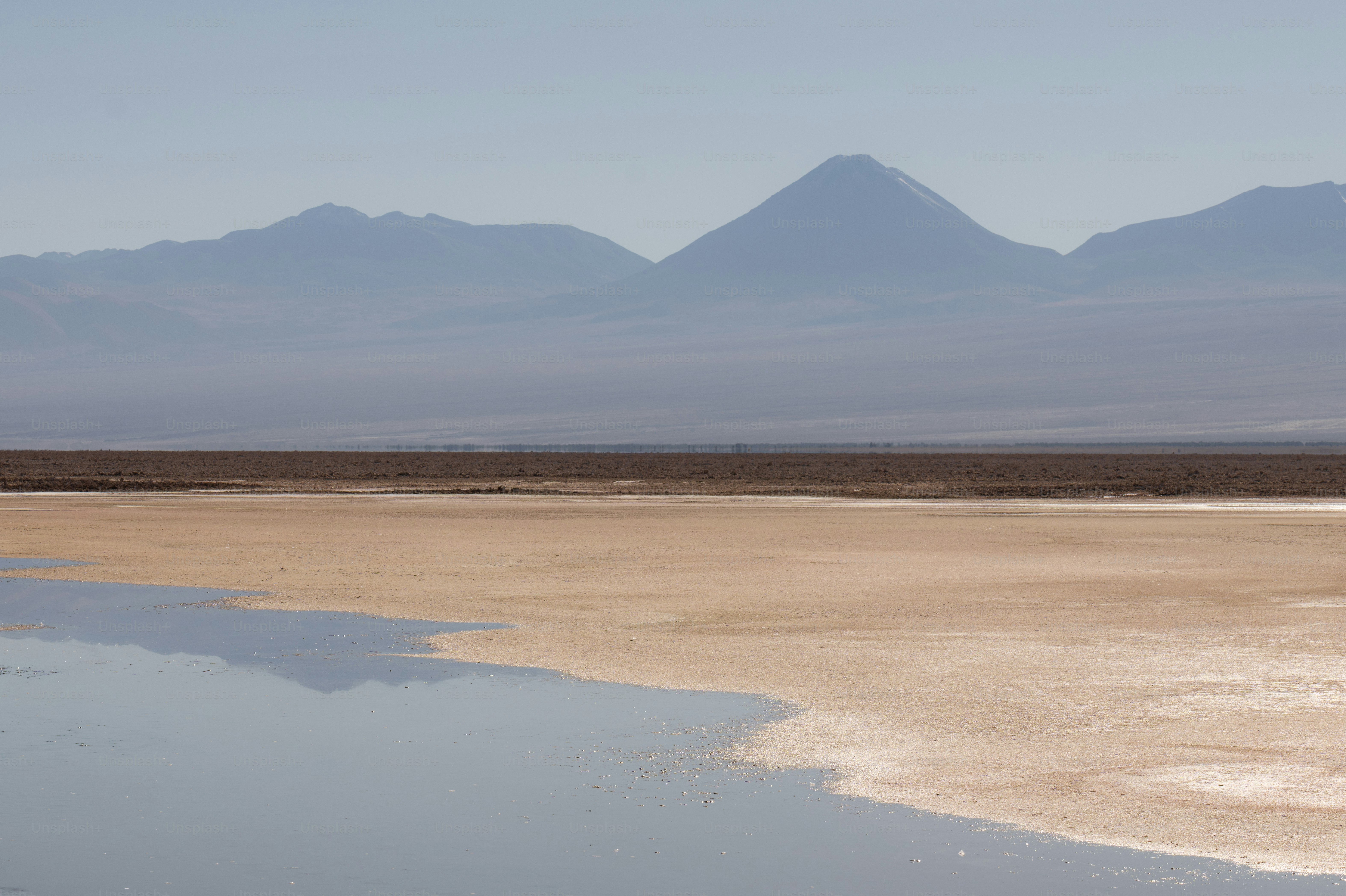 Montañas lejanas que se reflejan en aguas tranquilas y orilla arenosa