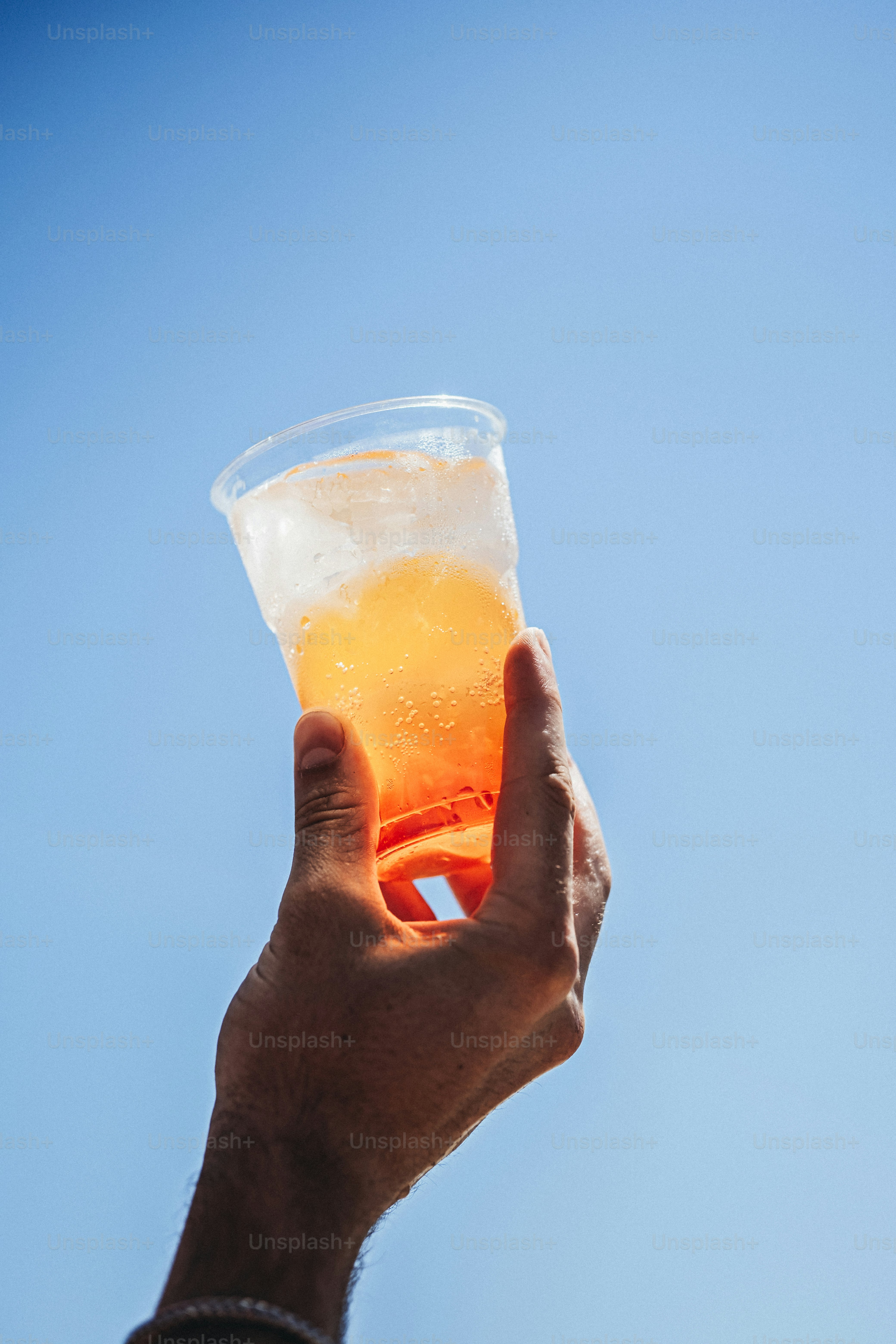 Hand holding orange drink with ice against blue sky
