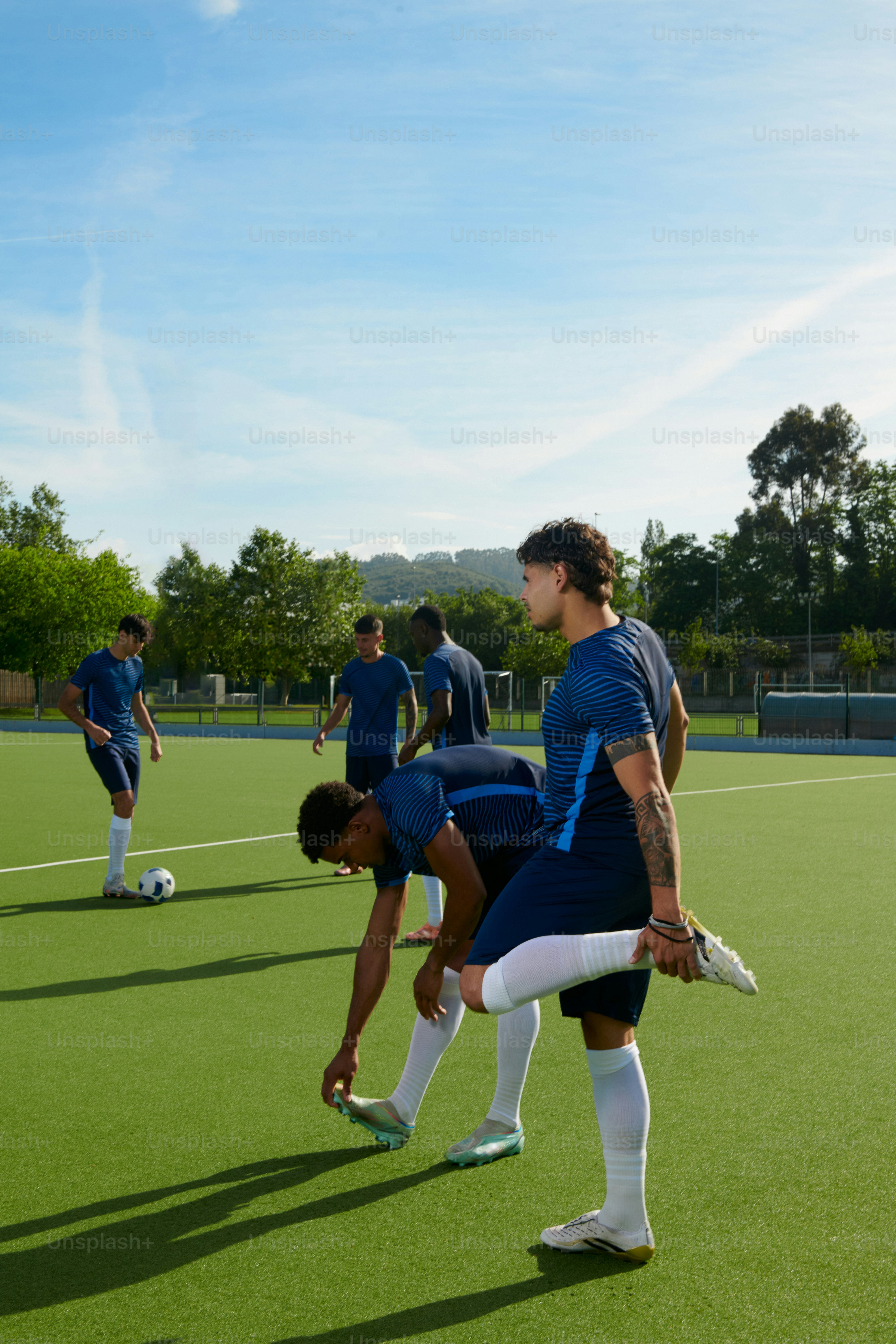Männliche Fußballspieler, die sich auf grünem Kunstrasen strecken.