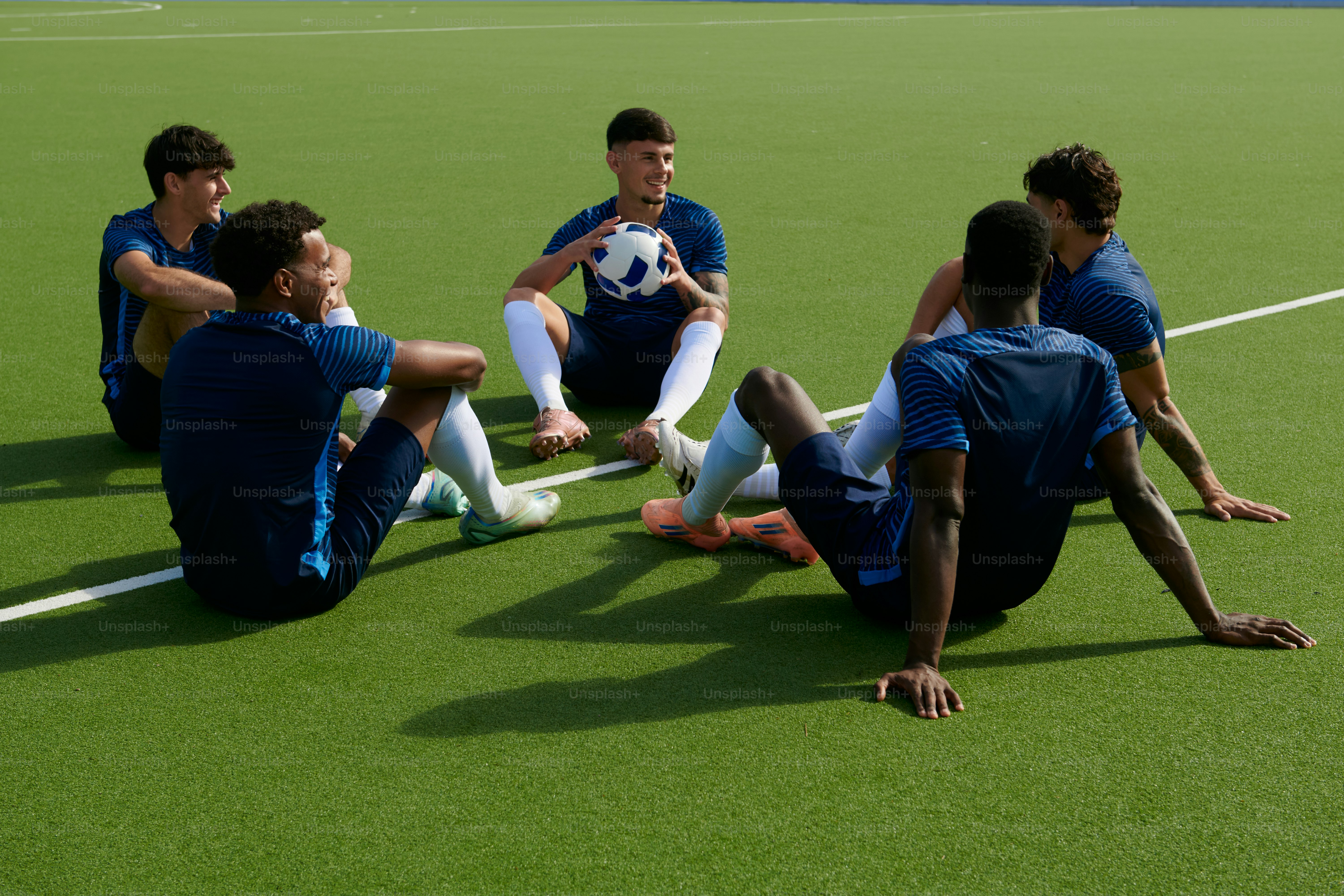 Junge Fußballspieler, die sich auf grünem Kunstrasen ausruhen