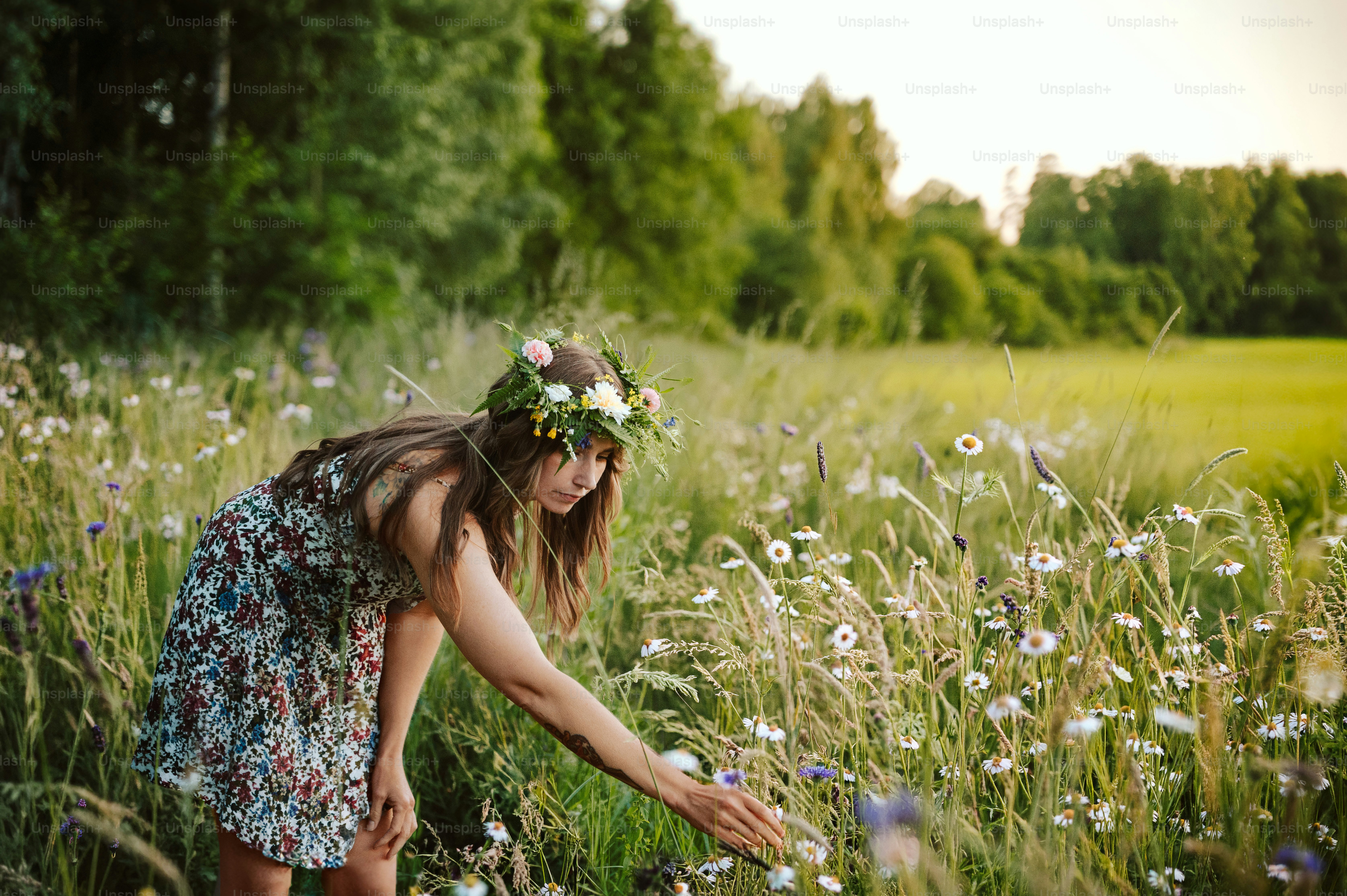 Frau mit Blumenkranz pflückt Wildblumen auf einer Wiese