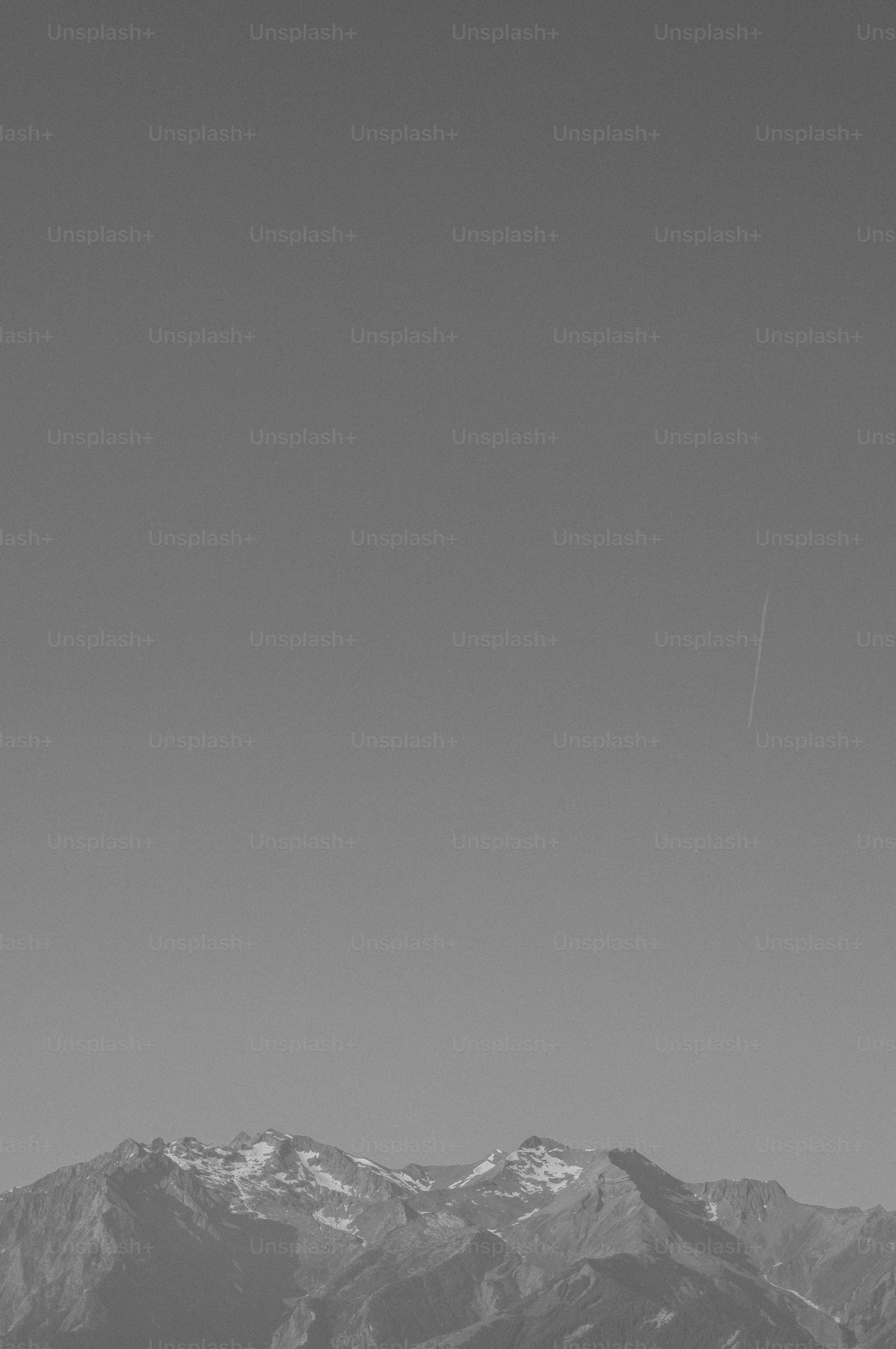 Monochrome snow-capped mountains under clear sky with contrail