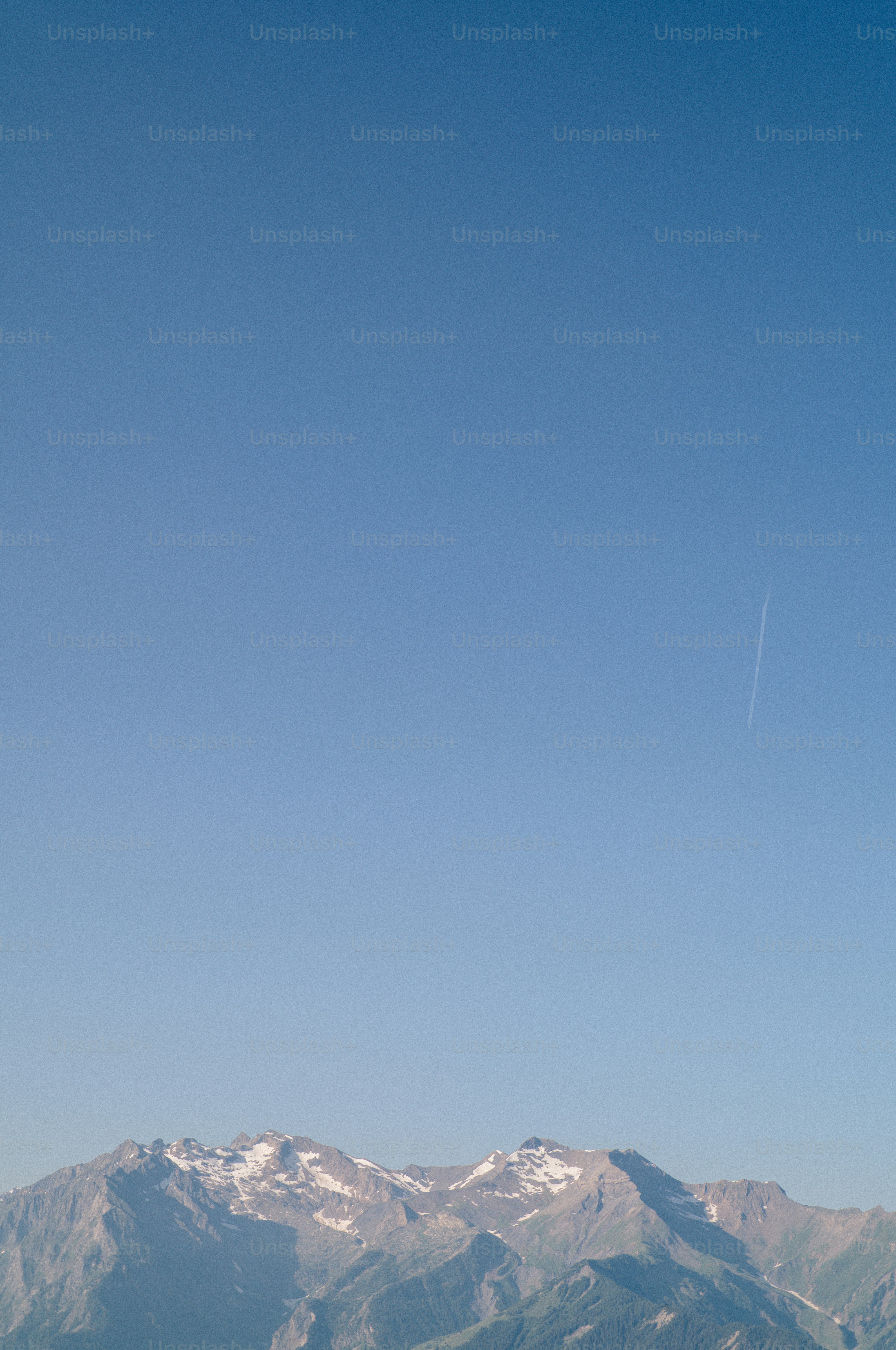 Snowy mountains under clear blue sky with contrail