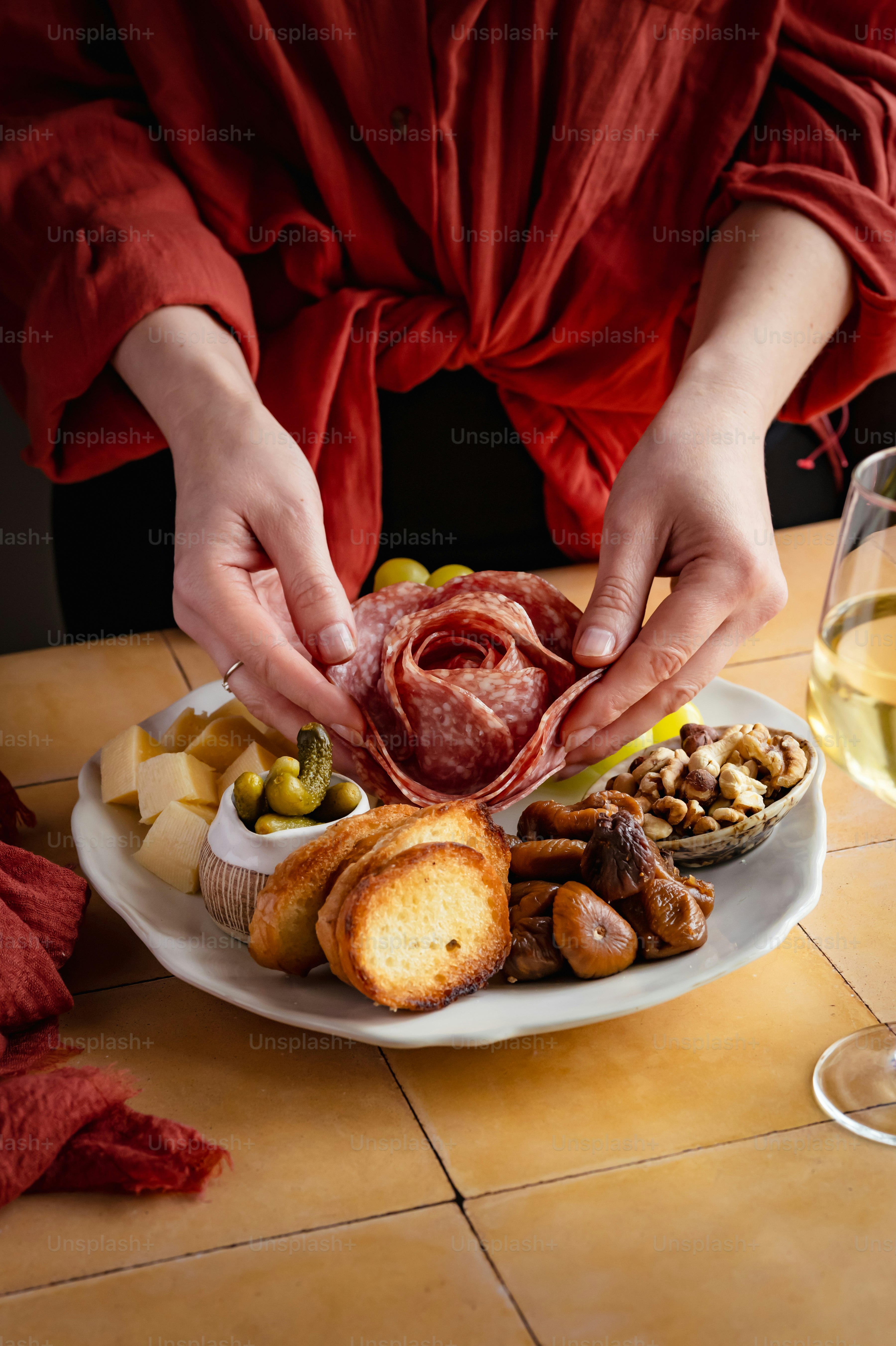 Hands arranging salami rose on charcuterie board