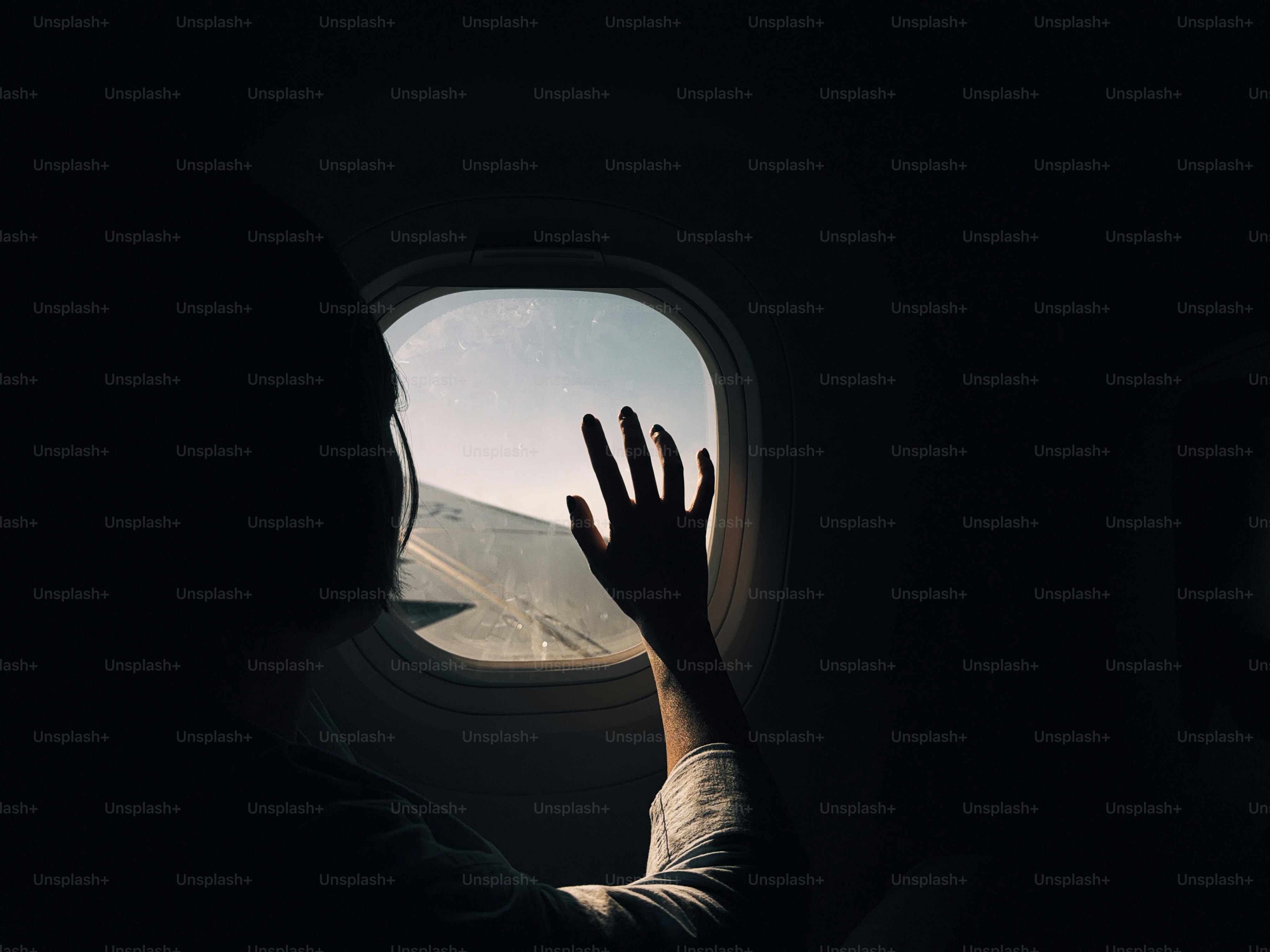 Person's hand touching airplane window during flight