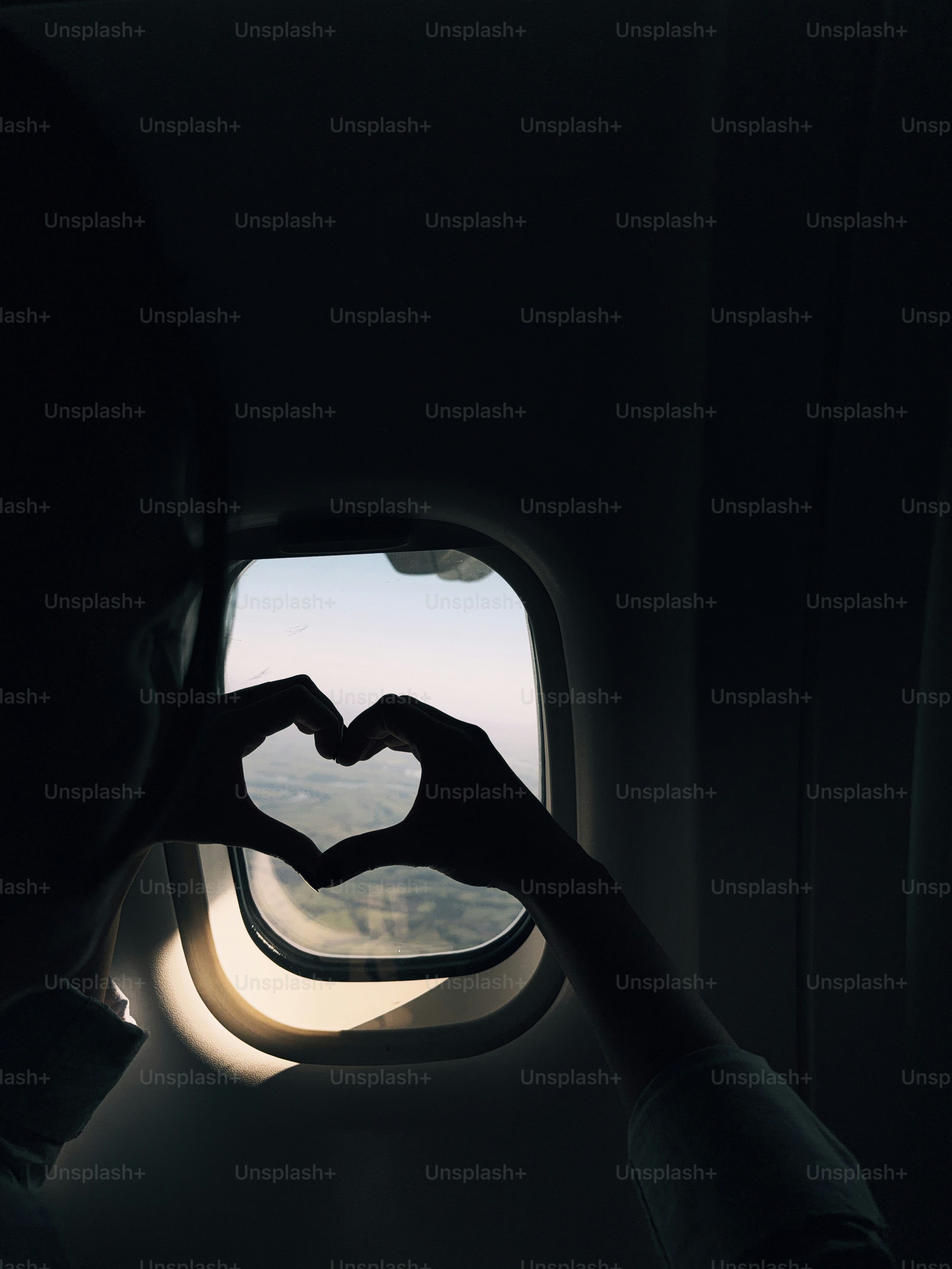 Silhouetted hands form heart shape against airplane window