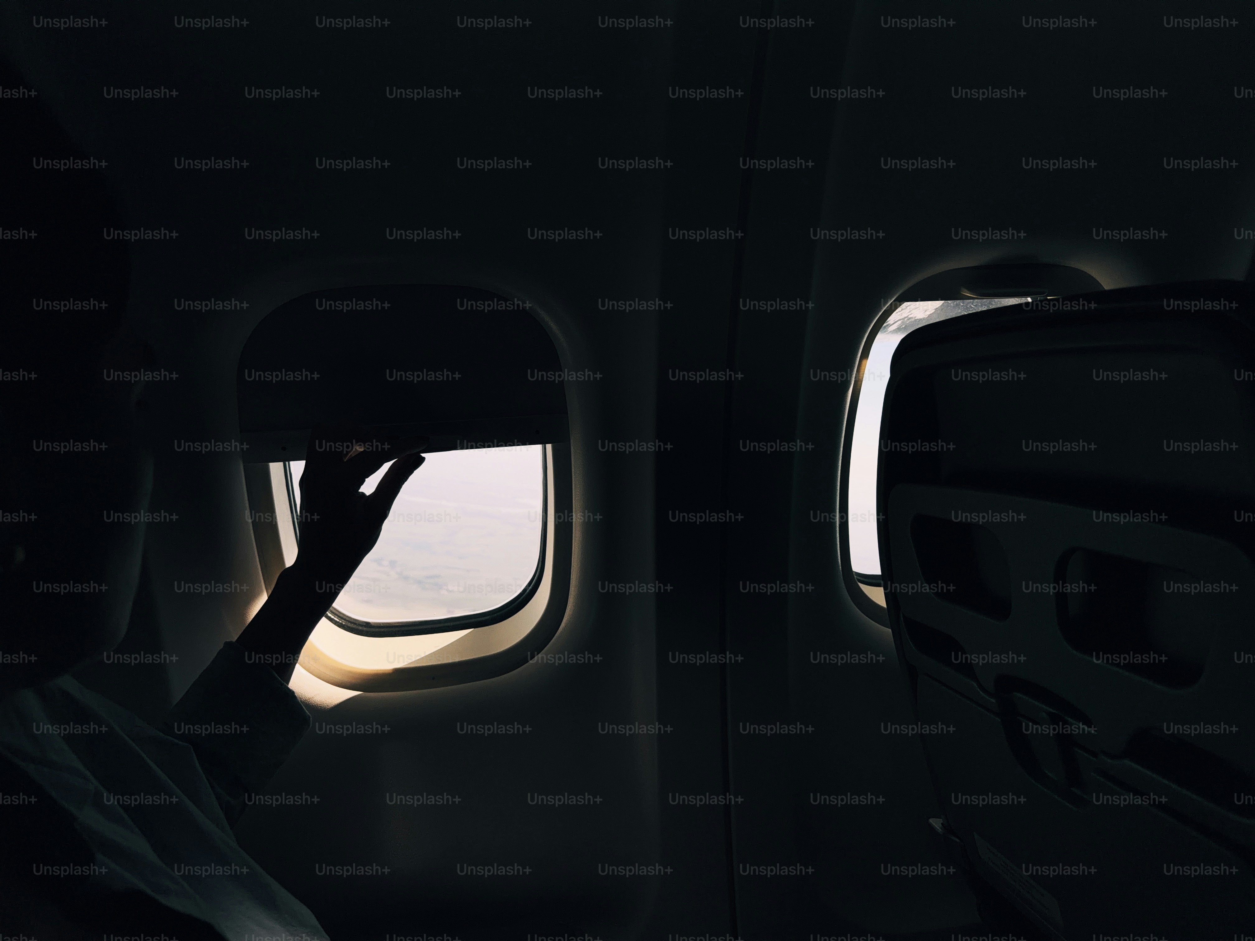 Hand adjusting window shade in dark airplane cabin