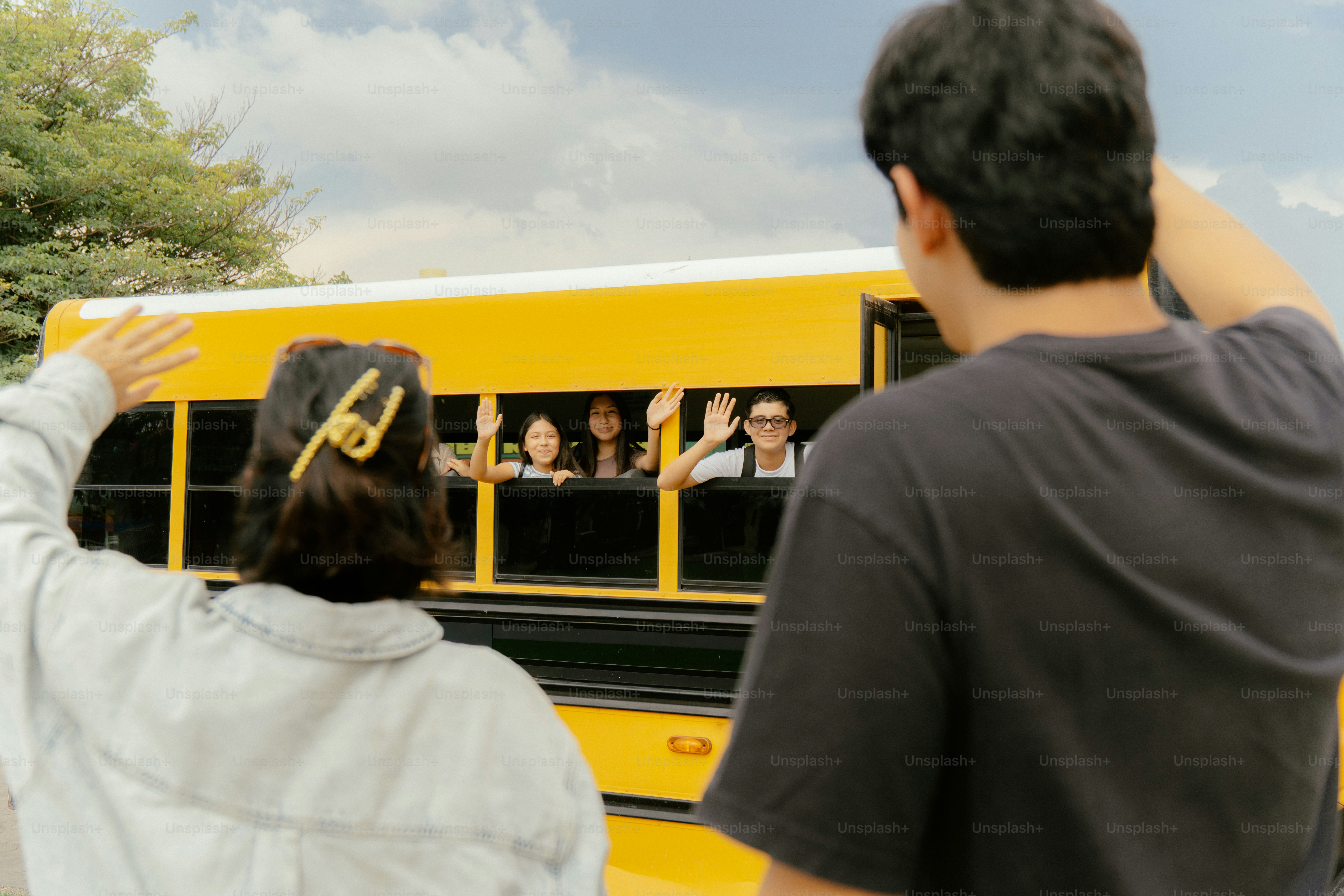 People waving to and from a yellow school bus