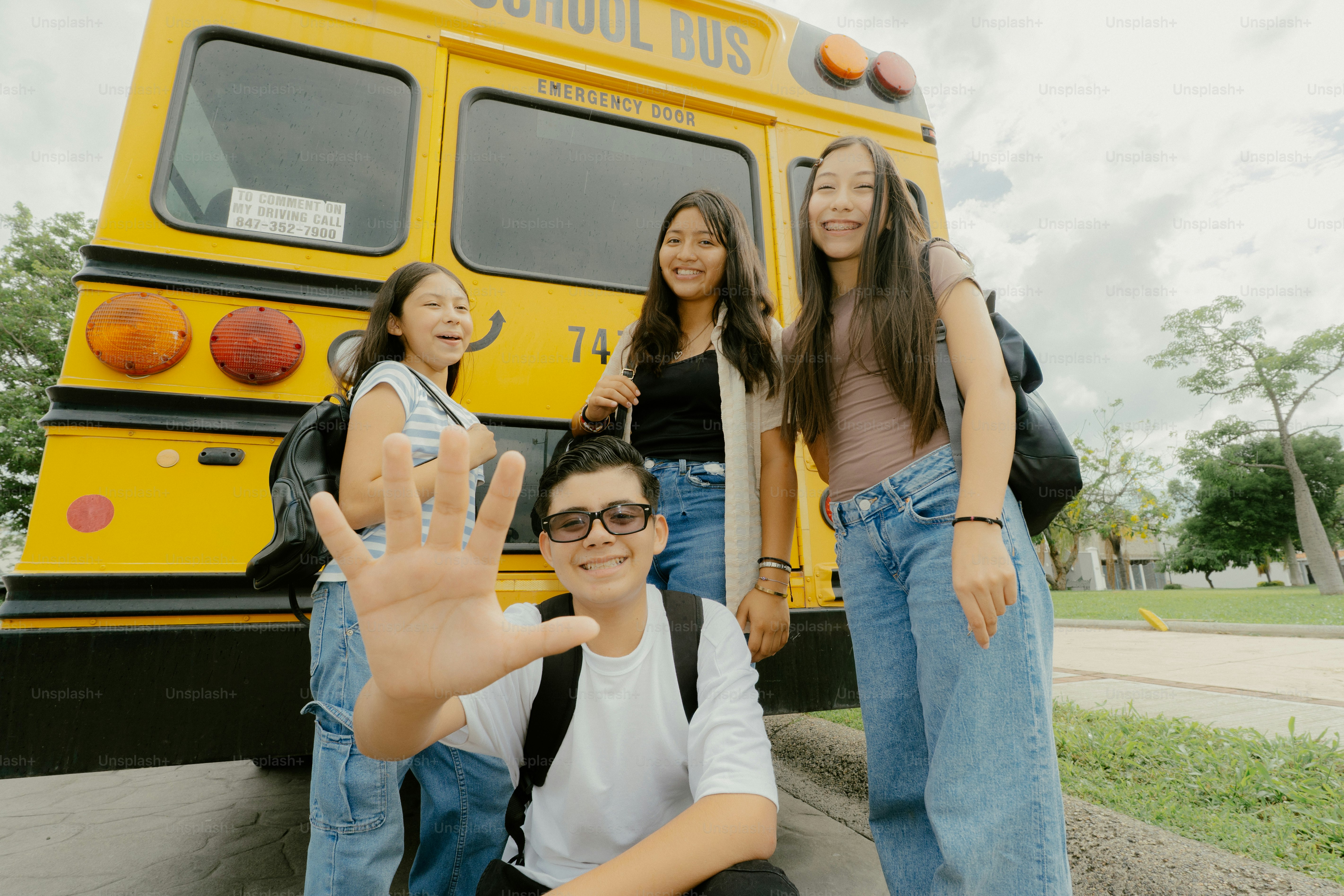 Students waving and smiling in front of school bus