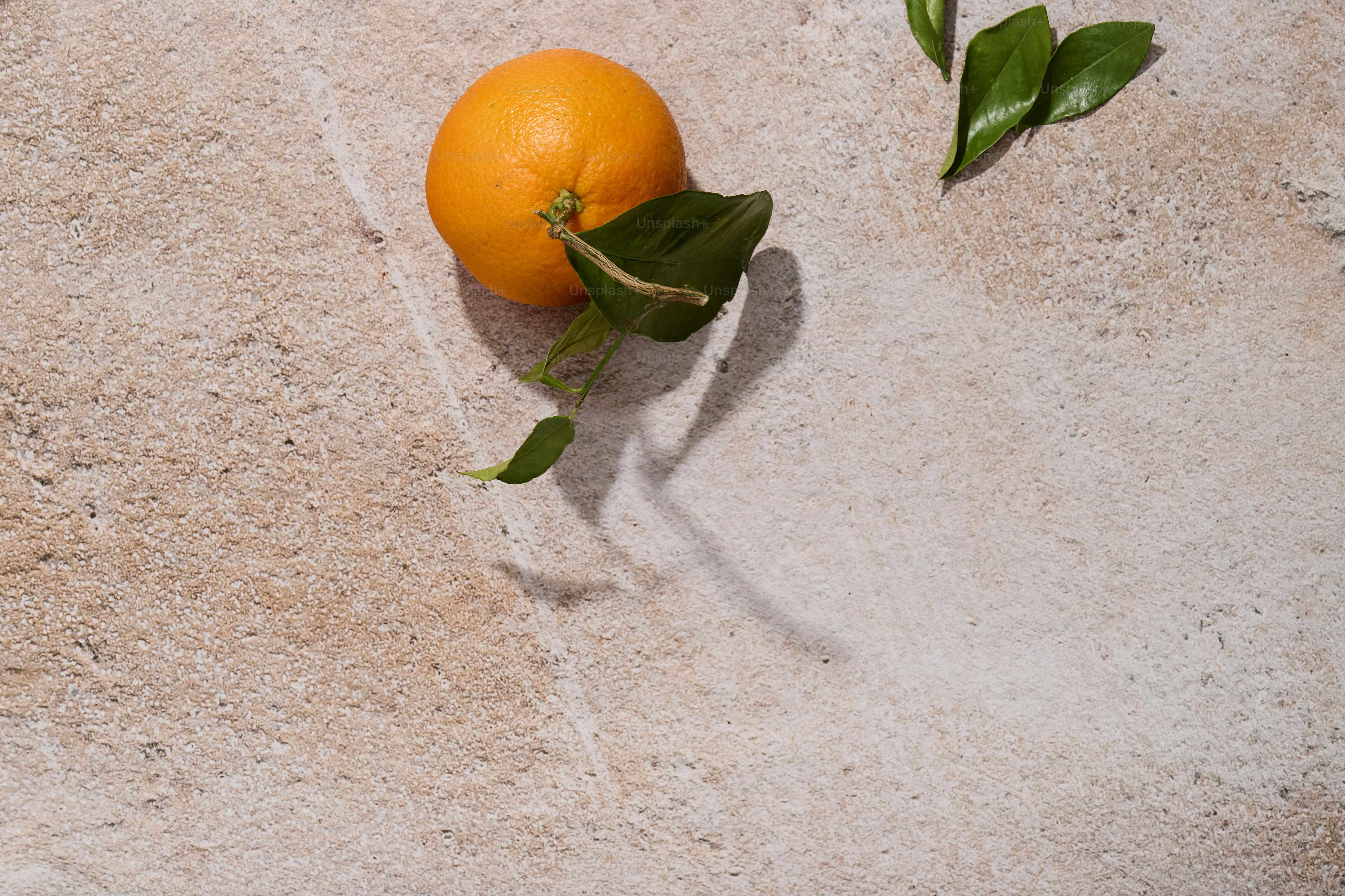 Orange with leaves on stone surface, bright sun