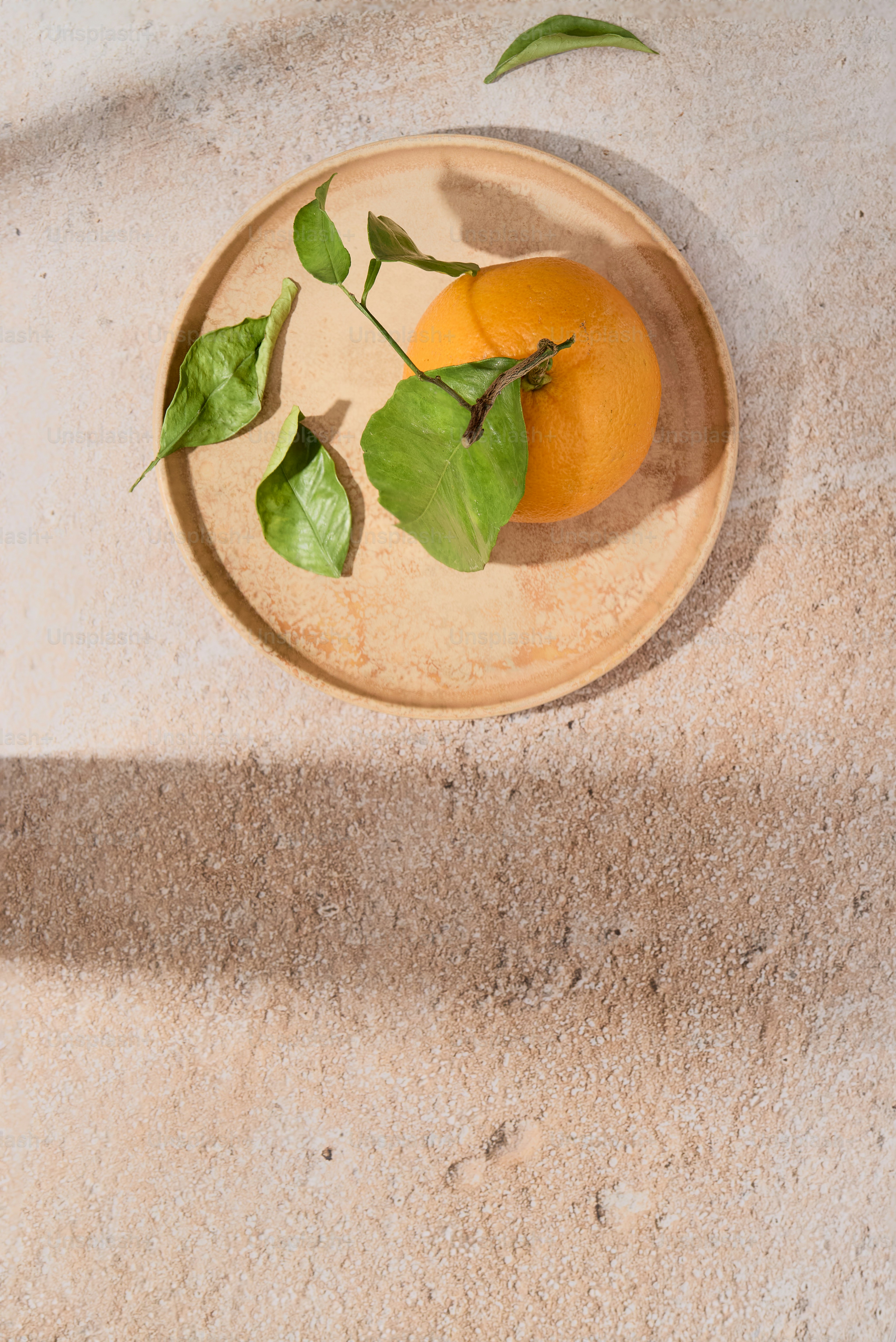 Orange with green leaves on plate, sunlit stone